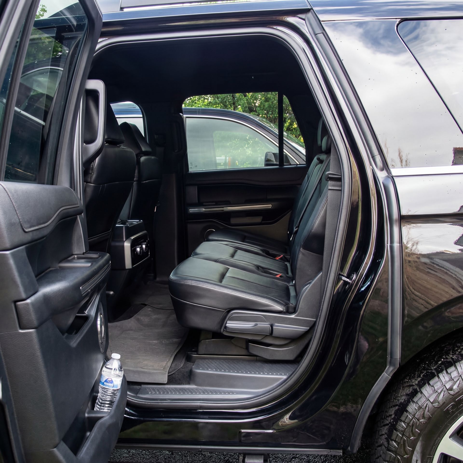 Black SUV's interior with open door, showing rear seats, dark leather, and water bottle in a side pocket.