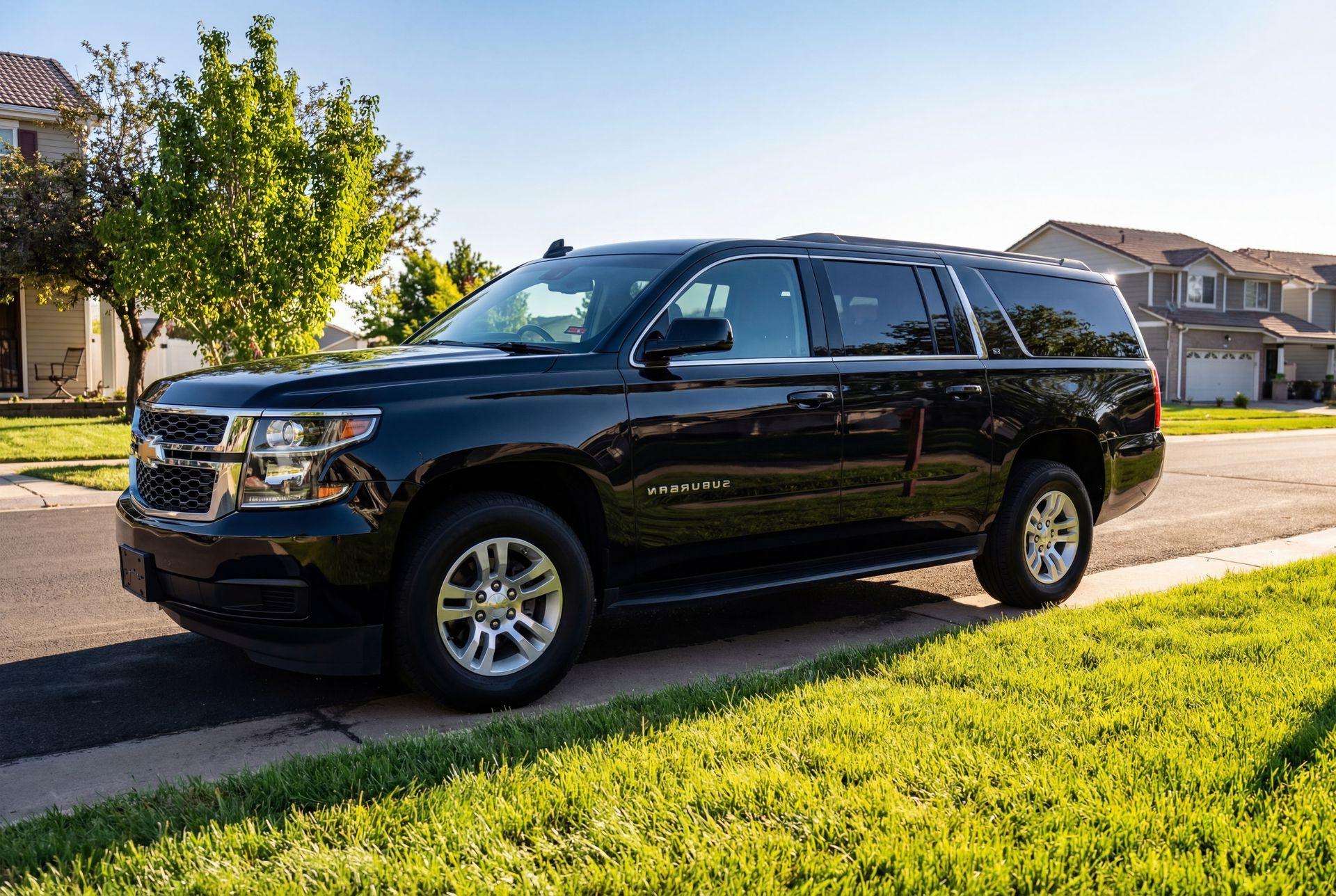 Black Chevrolet Suburban parked on a residential street with green grass and houses in the background.