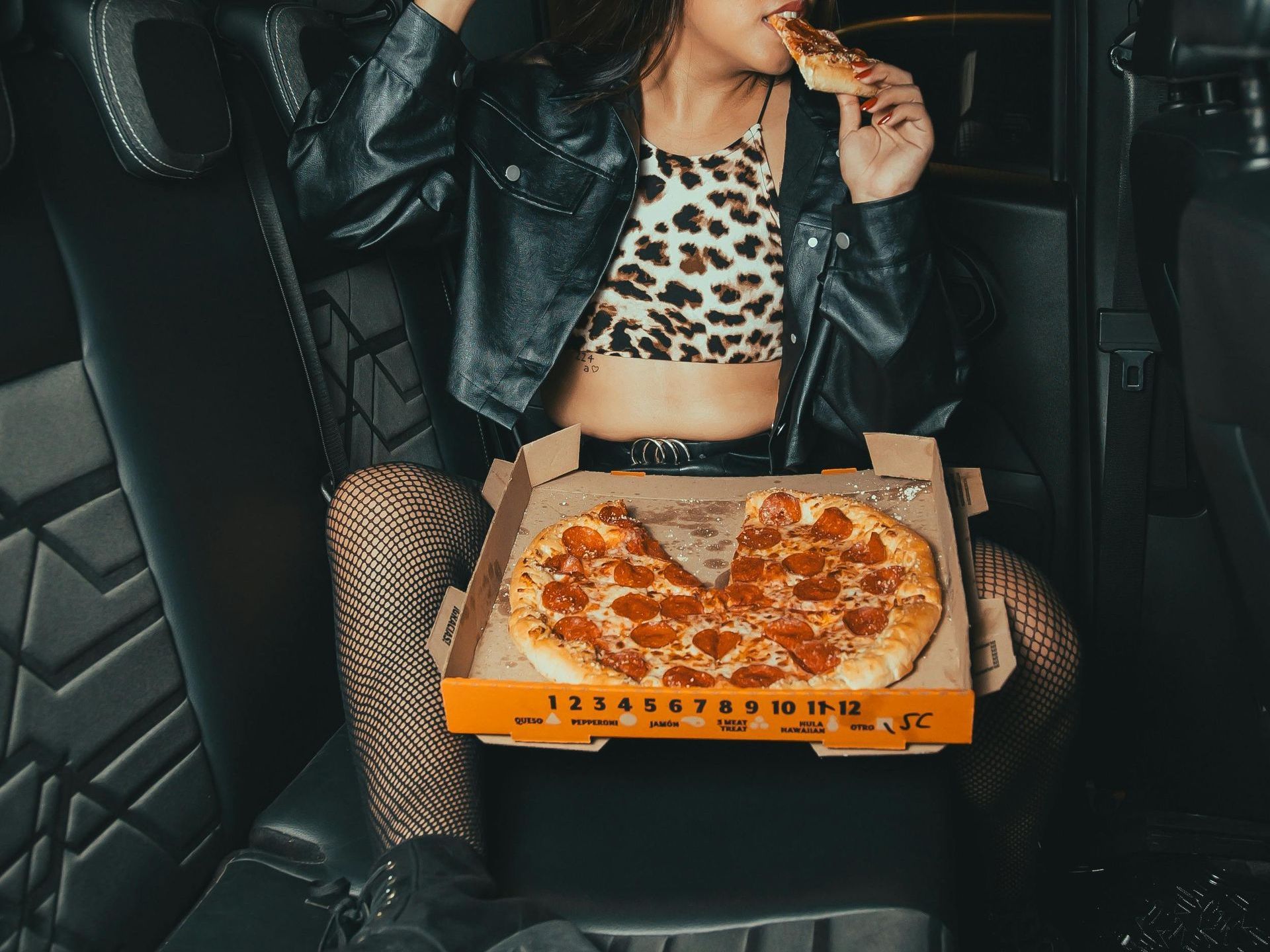 A woman is sitting in the back seat of a car eating a pepperoni pizza.