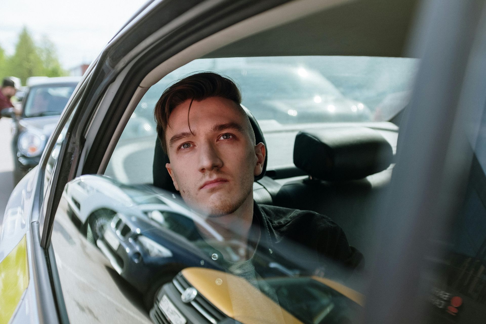 A man is sitting in the driver 's seat of a car looking out the window.