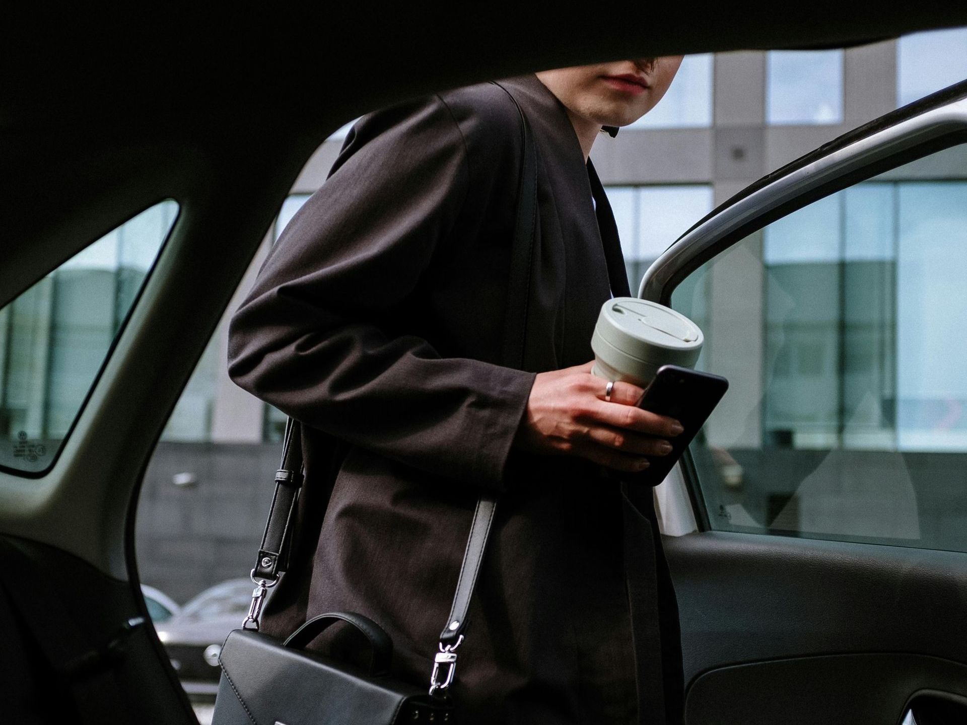 A man is getting out of a car holding a cup and a cell phone
