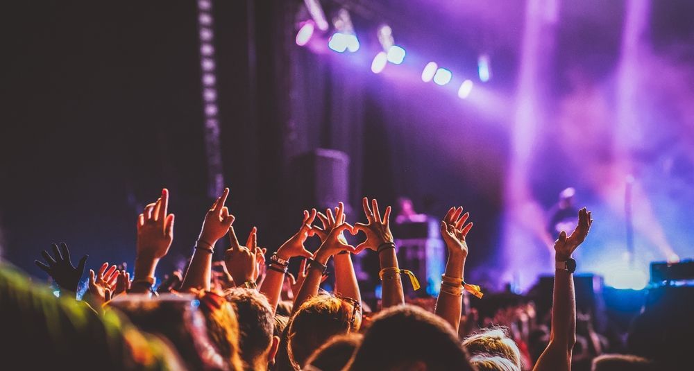 Crowd raising hands at a concert under purple stage lights and haze