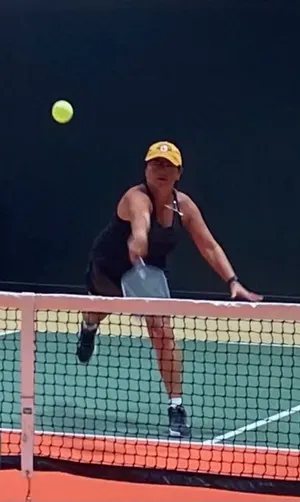 Tennis player lunging at the net to volley a yellow ball on an outdoor court