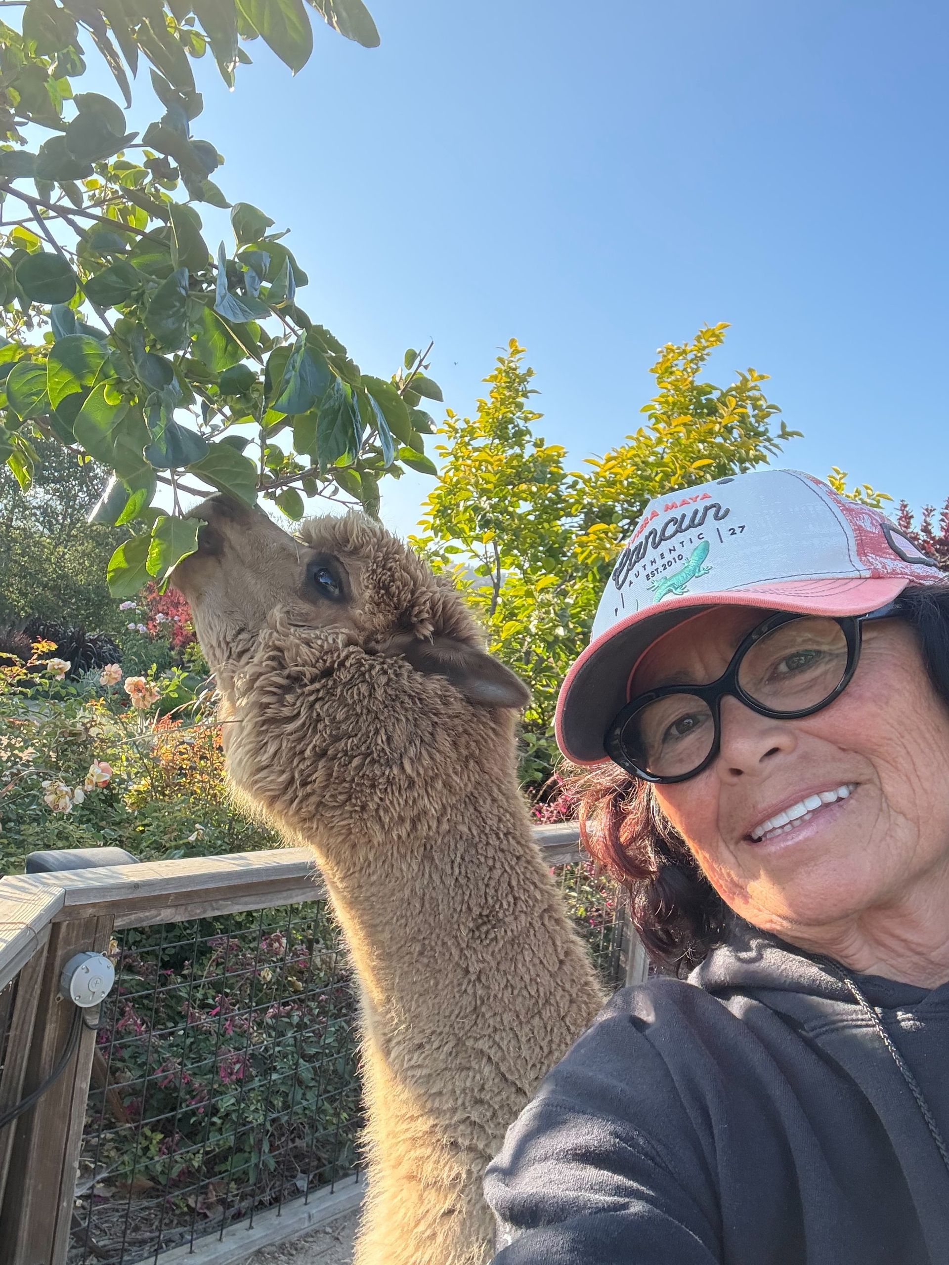 Smiling woman in glasses and cap taking a selfie beside a squirrel on a branch outdoors