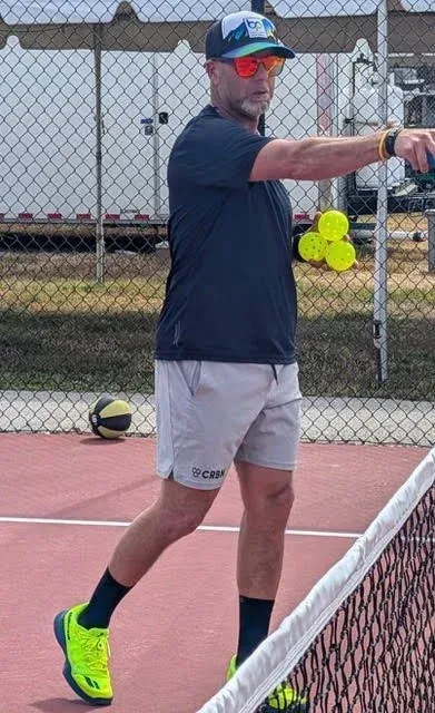 Tennis player in navy shirt and gray shorts holds a forehand on an outdoor court.