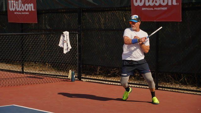 Tennis player in white and blue warms up on a clay court beside Wilson signs.