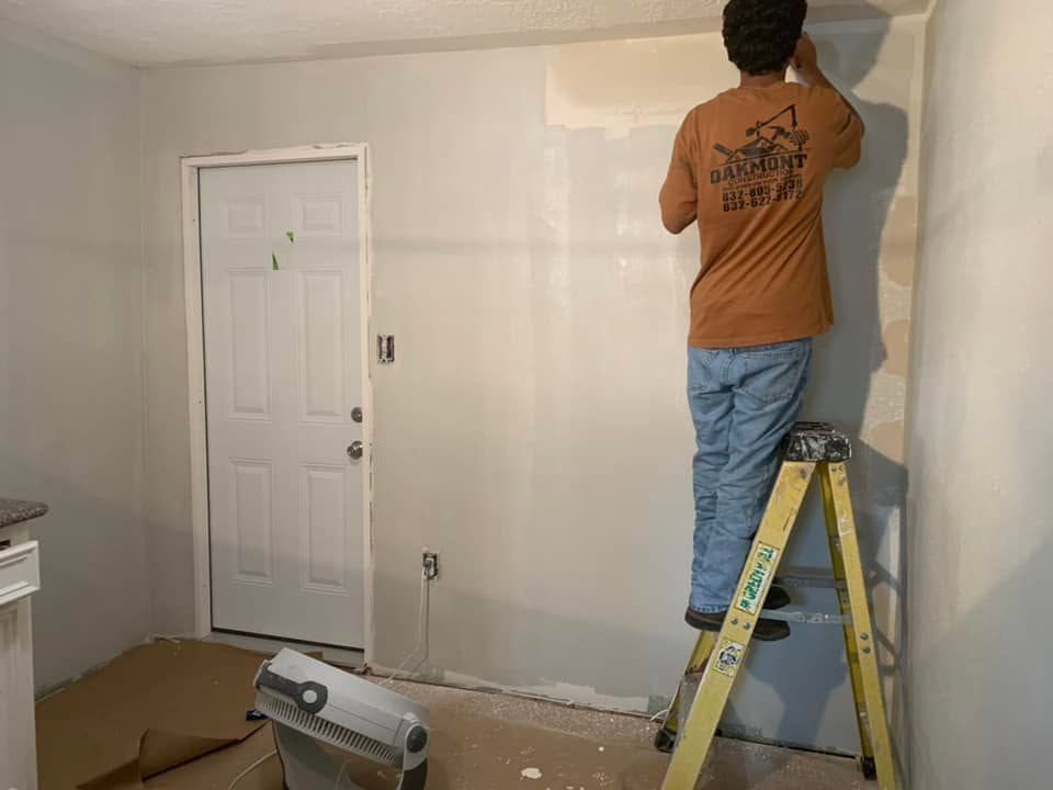 Person painting a wall above a ladder in a room with white walls and a door