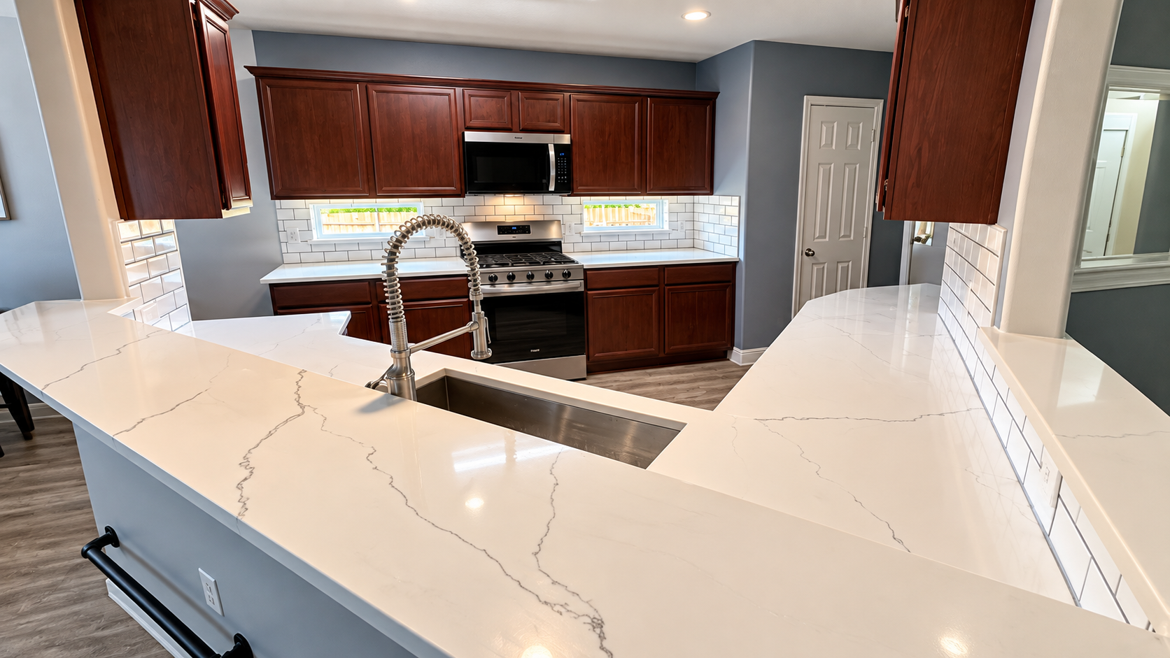 Modern kitchen with white marble island, dark wood cabinets, stainless appliances, and pendant lights