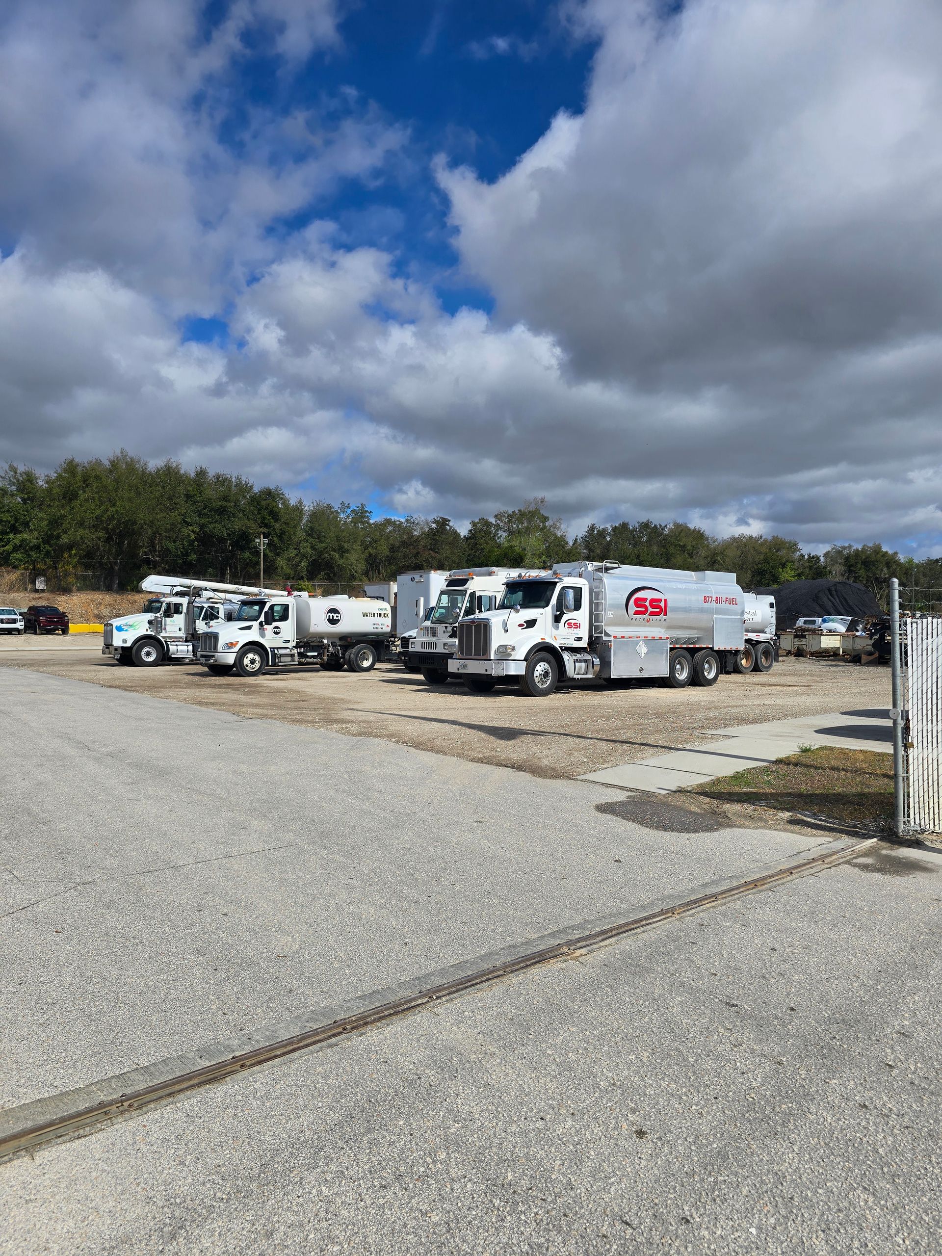 White utility trucks parked on a gravel lot under a cloudy sky.