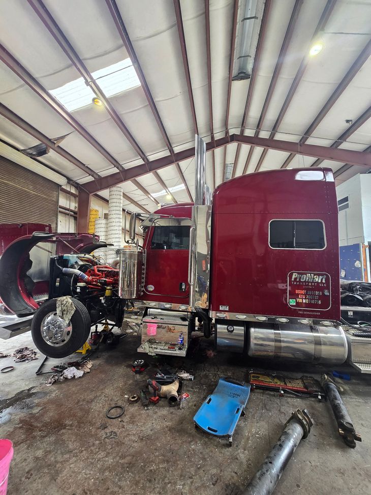 Red semi-truck in a repair bay with tools and parts scattered on the floor