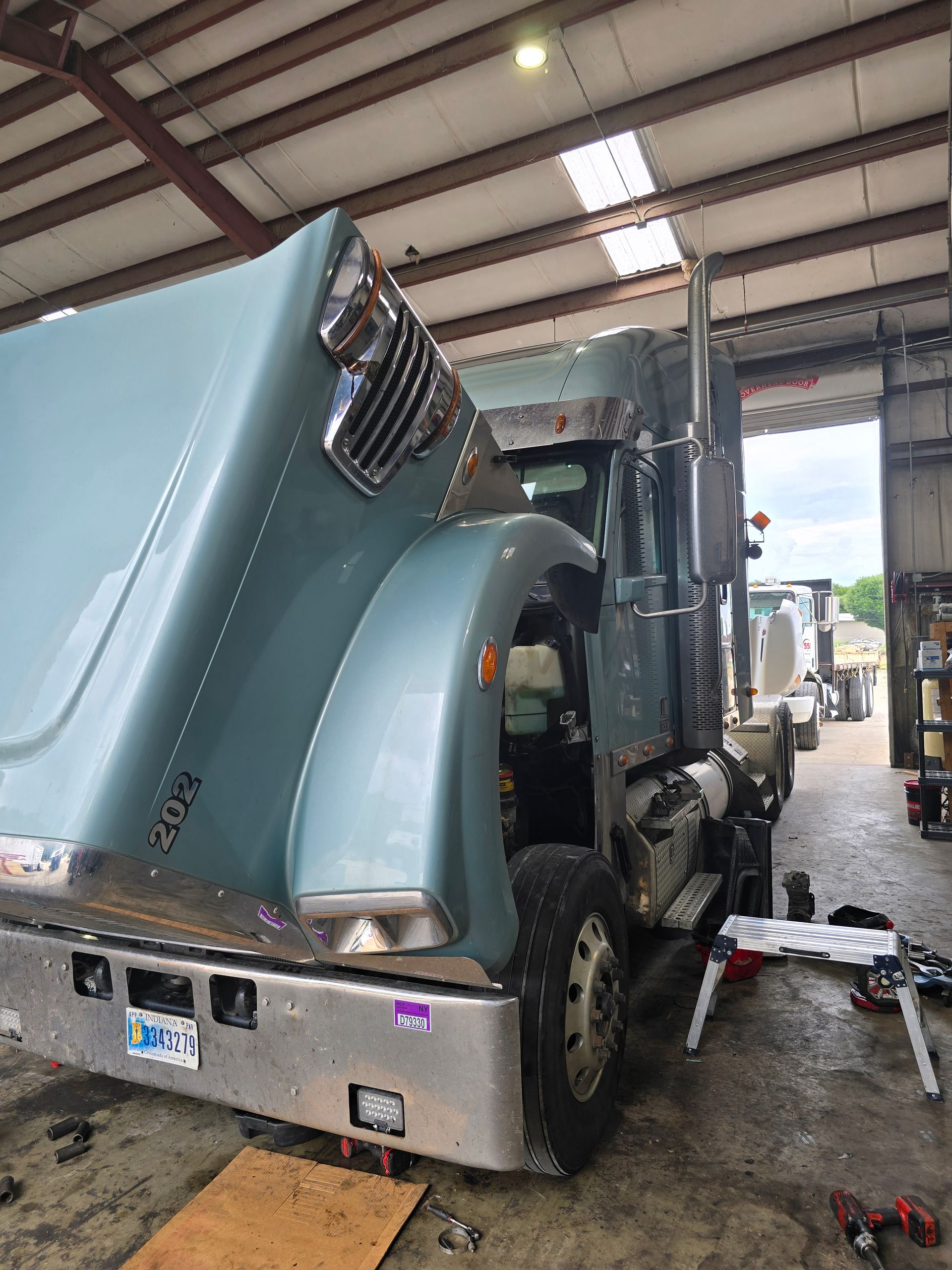 Blue semi-truck inside a garage, seen from the rear with the cab tilted forward for maintenance