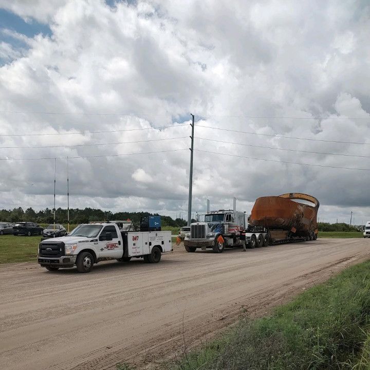 Tow truck hauling a rusted dump trailer on a gravel road under cloudy skies