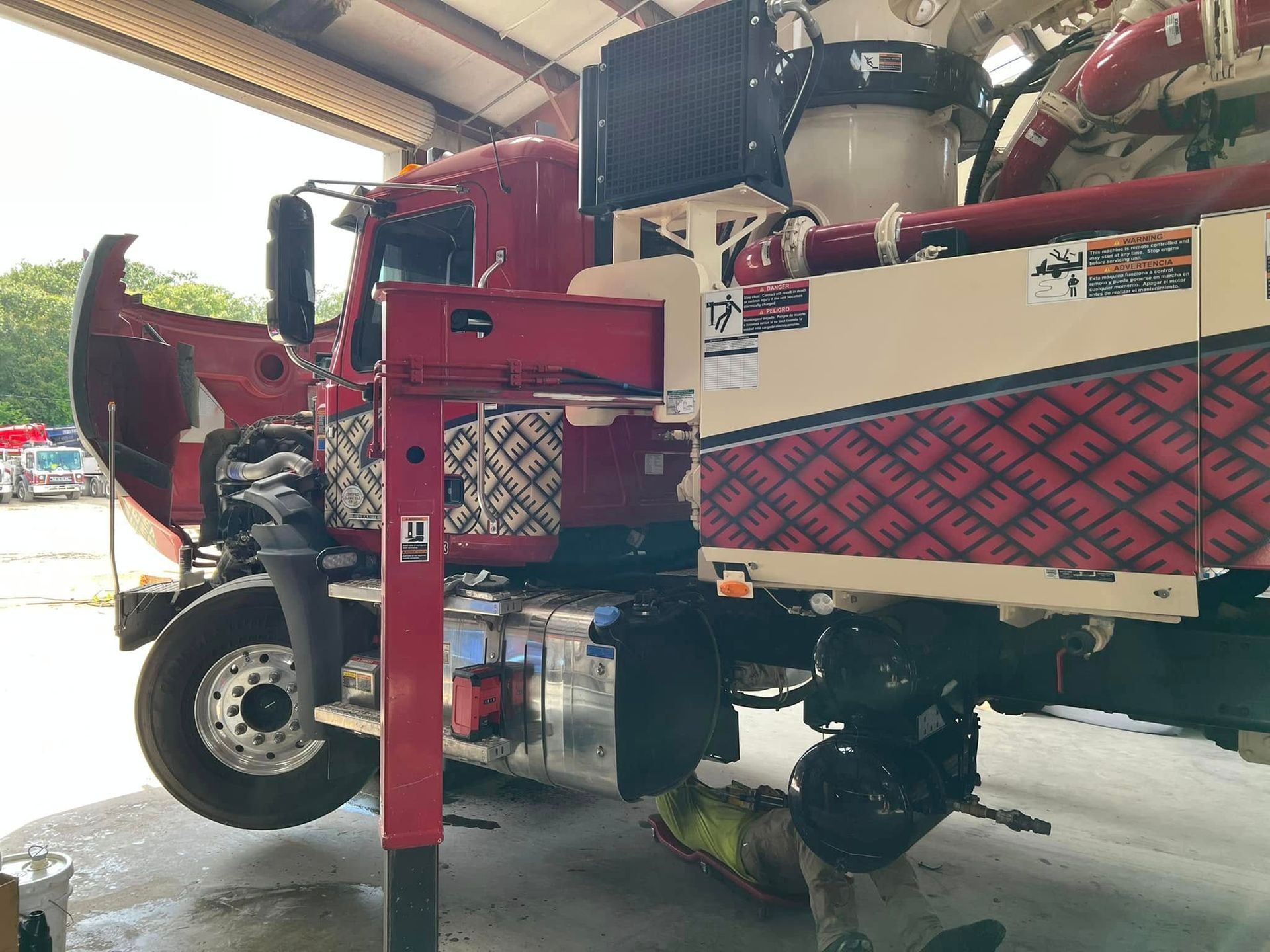 Red agricultural sprayer parked under a shed, with large wheels and red booms folded in.