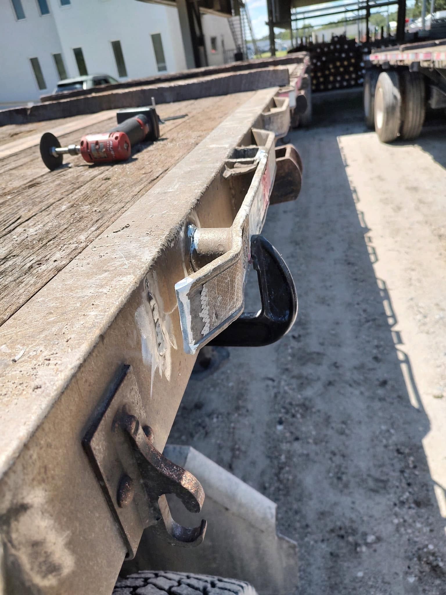 Flatbed trailer corner with white hydraulic hose and metal fittings in an industrial yard