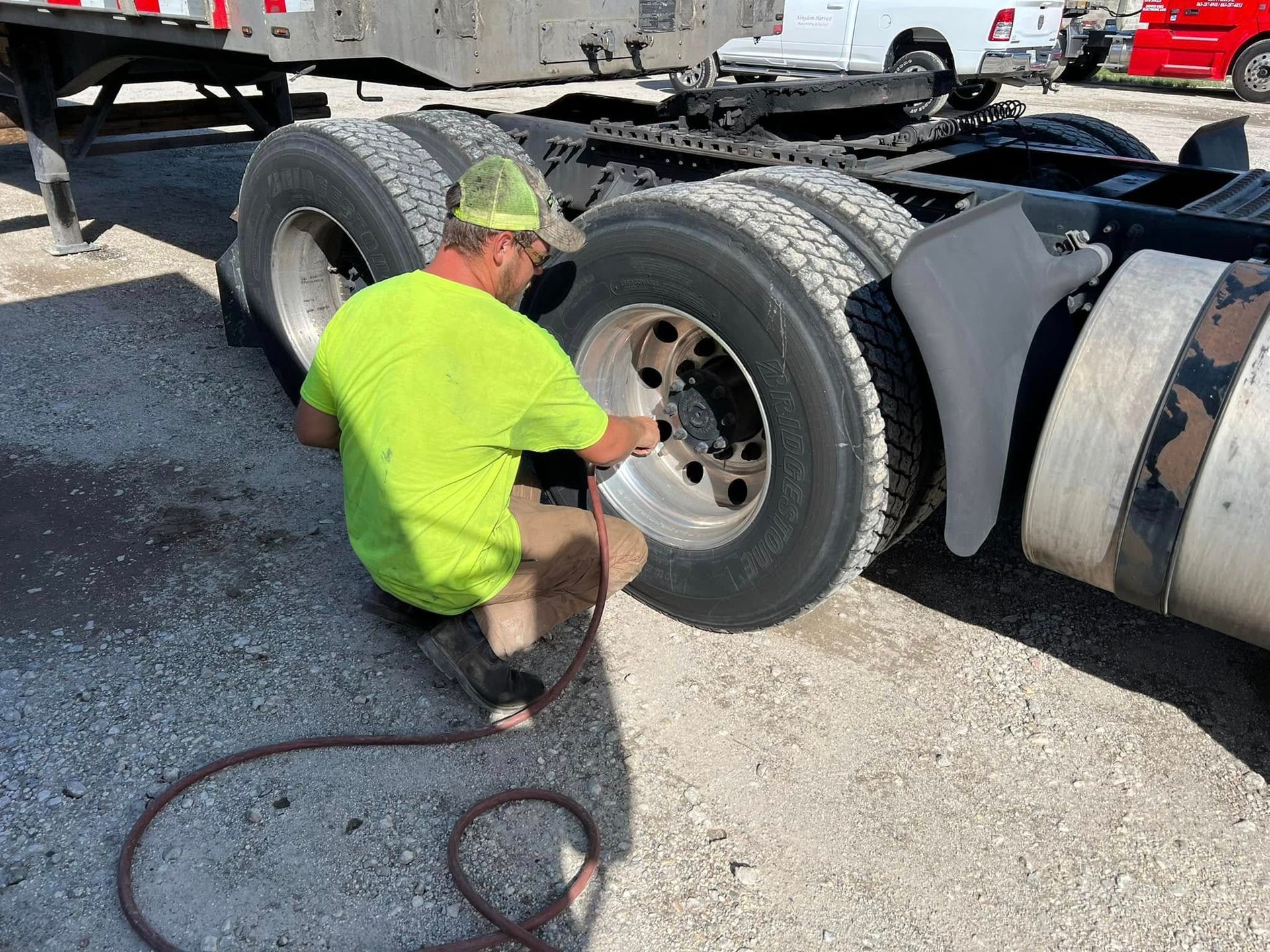 Worker in neon shirt kneels by a truck wheel, using an air hose to inflate the tire.