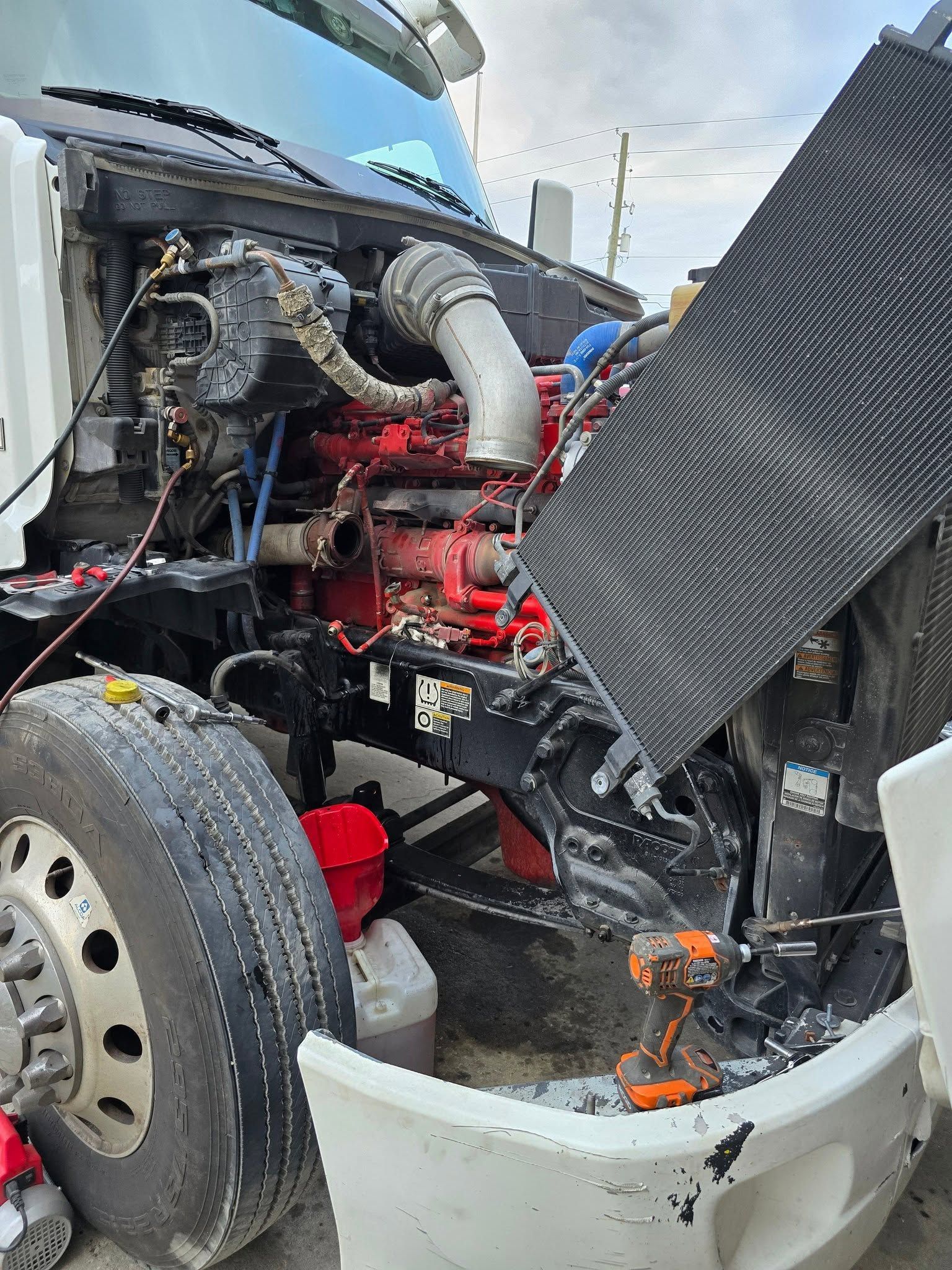 Damaged semi-truck engine bay with exposed red engine and bent front bumper after a collision