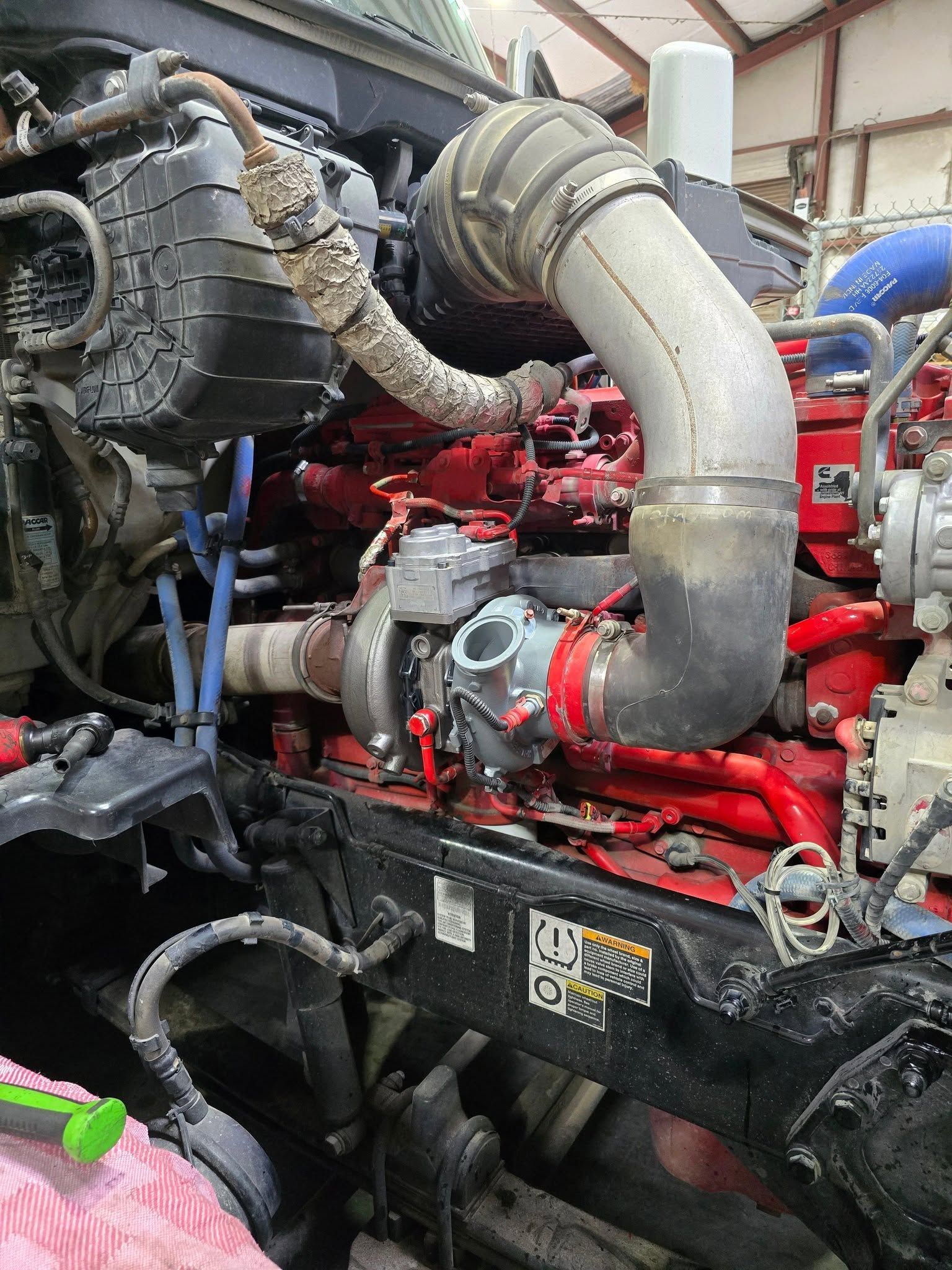 Engine compartment with red machinery, large gray hose, and black components in an industrial setting
