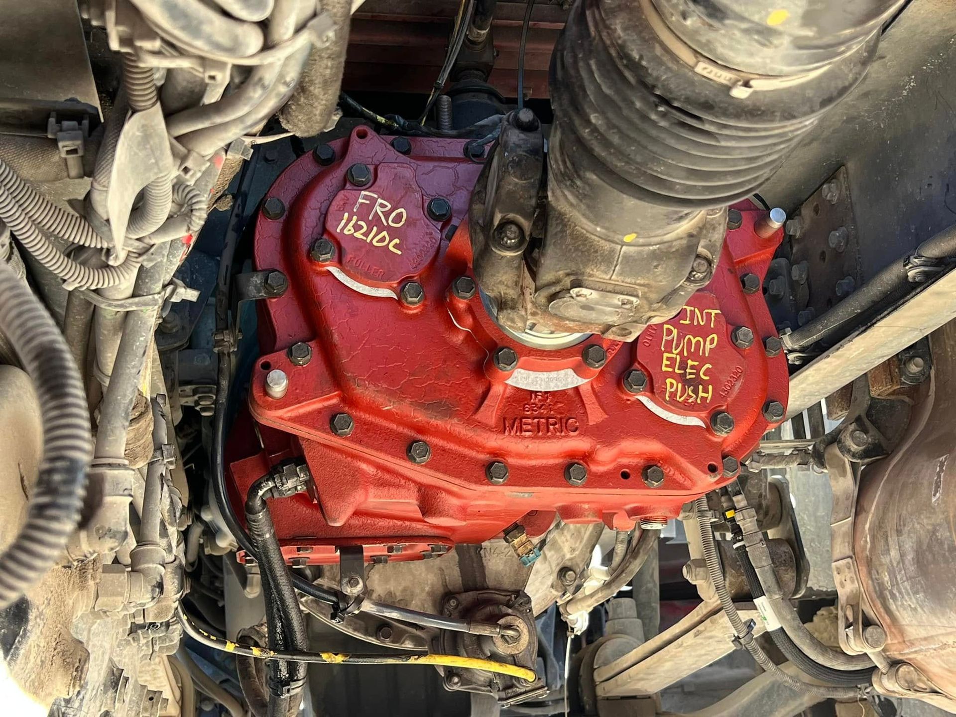 Red-painted mechanical gearbox or engine assembly with hoses and wiring in an industrial setting