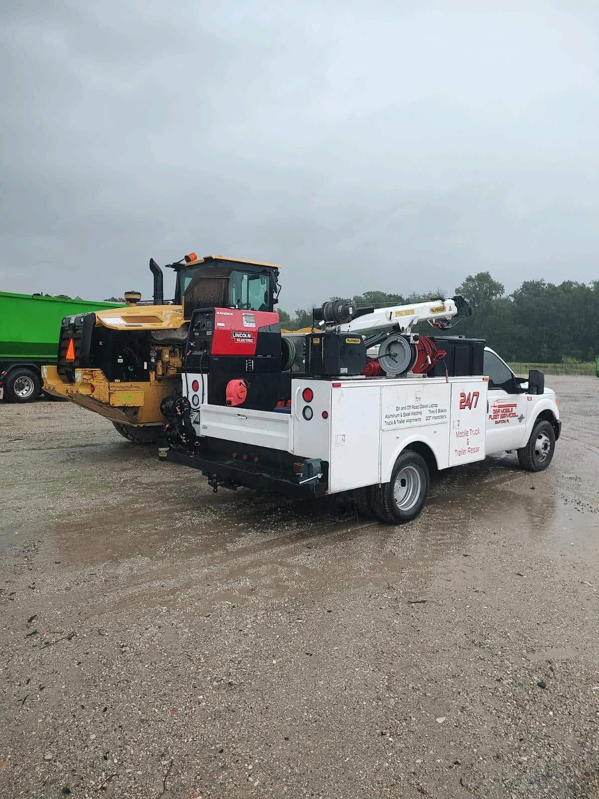 White tow truck carrying a yellow tractor on a gravel lot under a cloudy sky