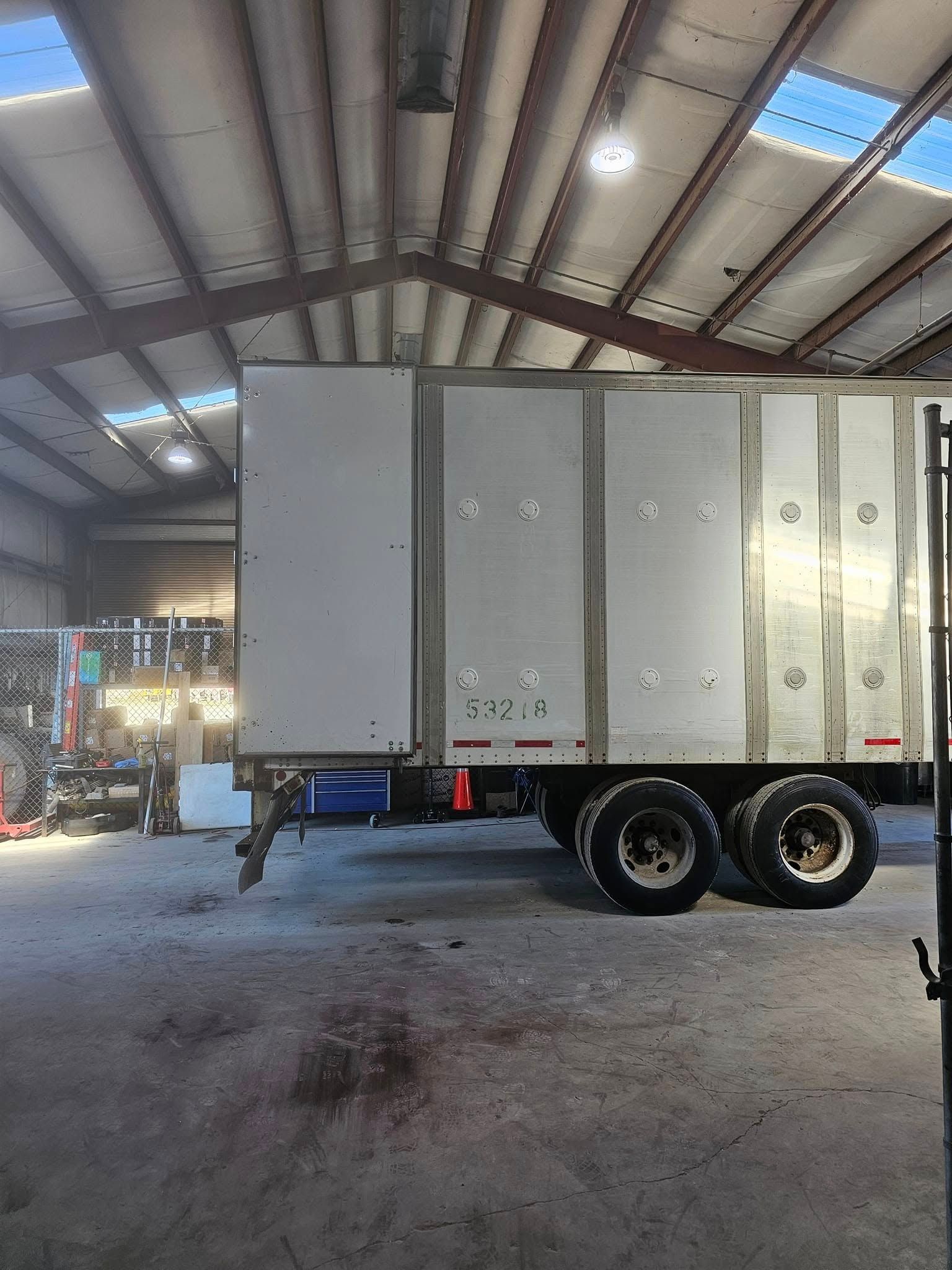 White box trailer inside a warehouse, shown side-on with dual rear wheels and metal roof overhead.