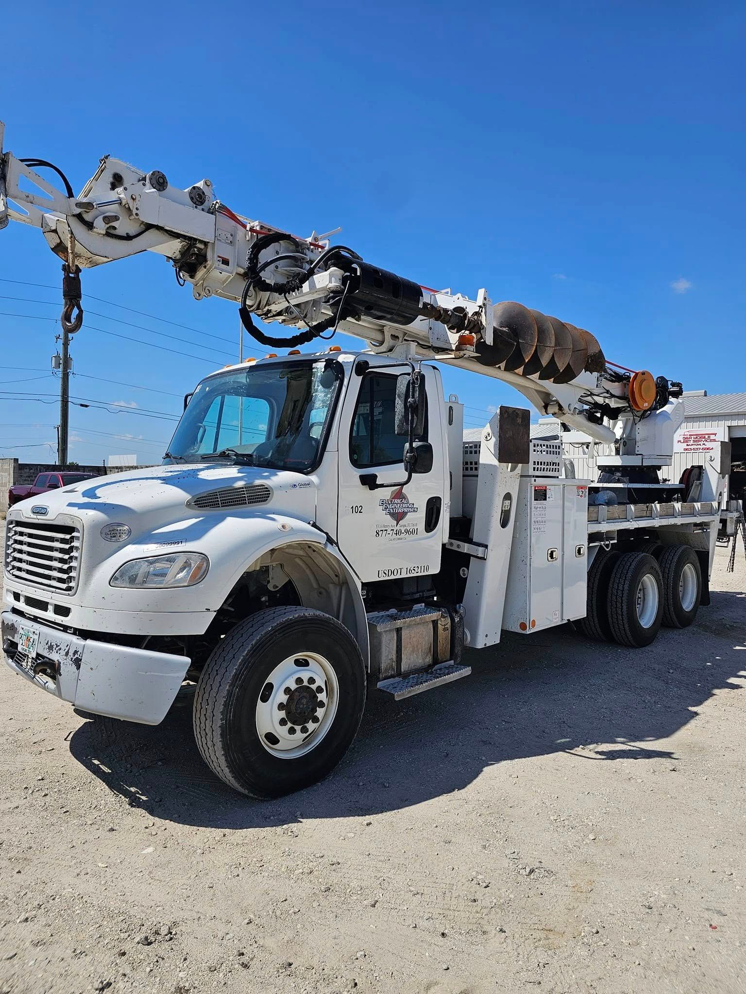 White utility truck with a boom lift parked on gravel under a clear blue sky.
