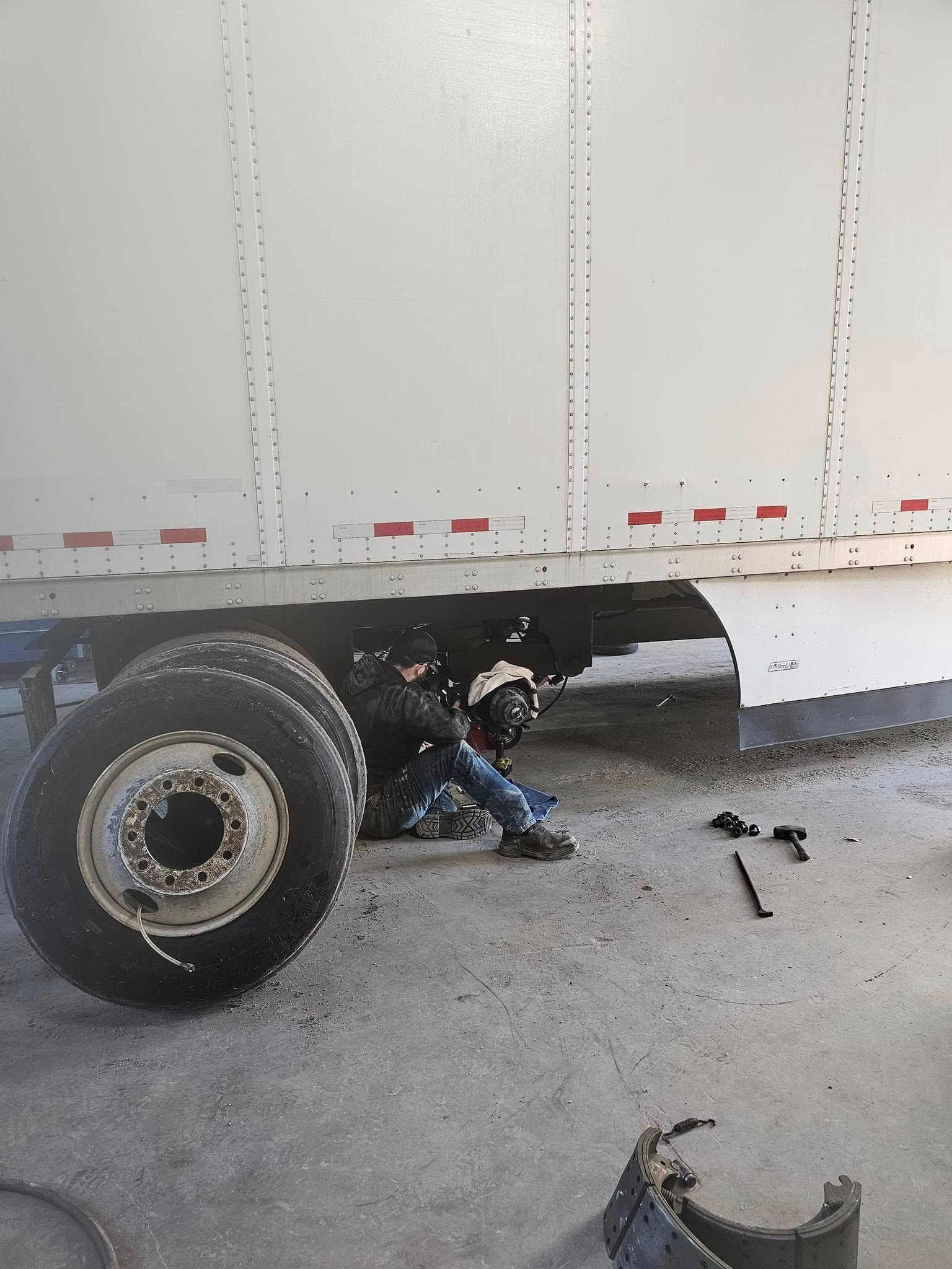 Person working under a white truck near the rear wheel, with tools on the pavement.