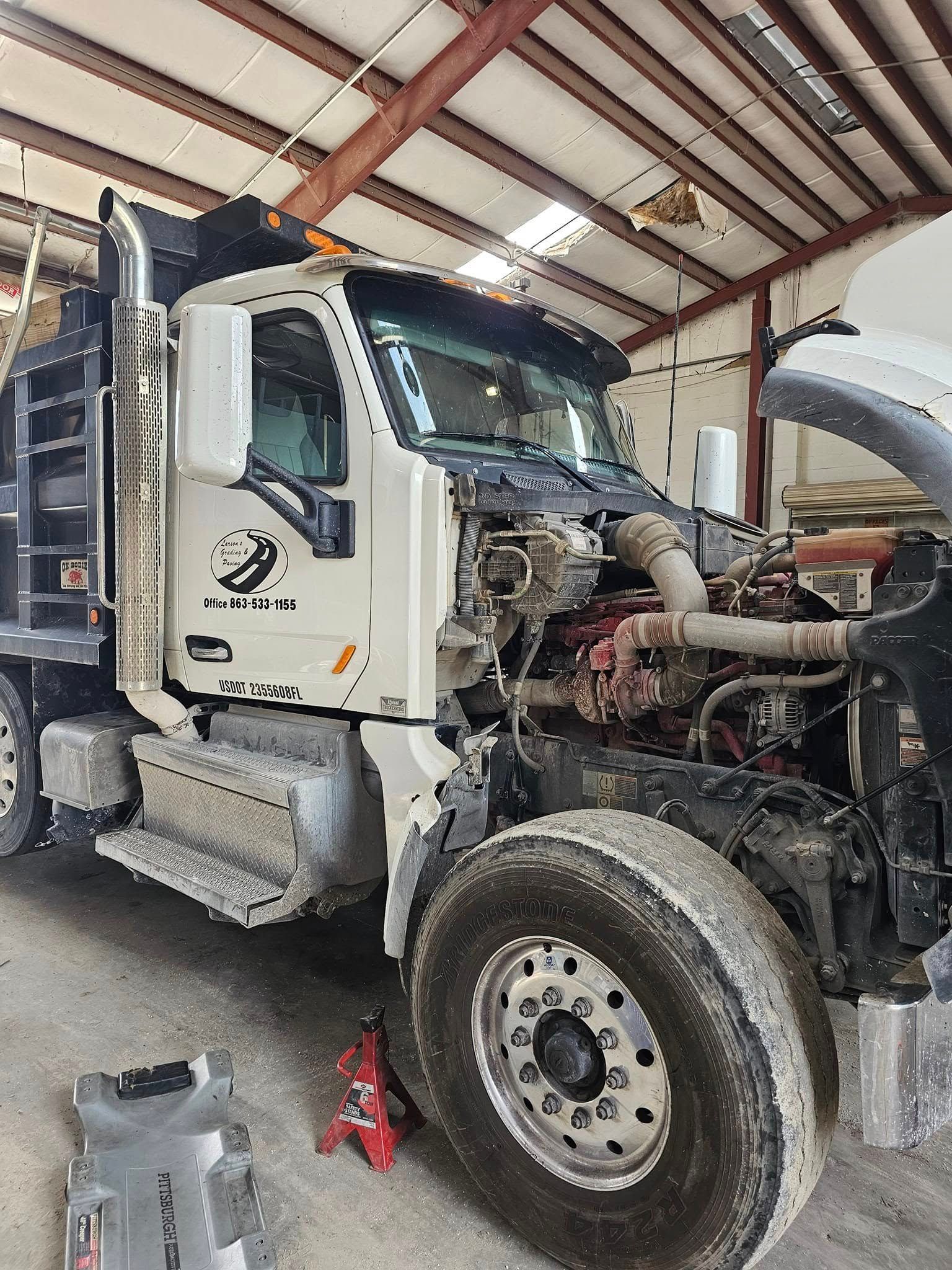 White semi-truck in a garage, front end exposed for repairs with engine visible.