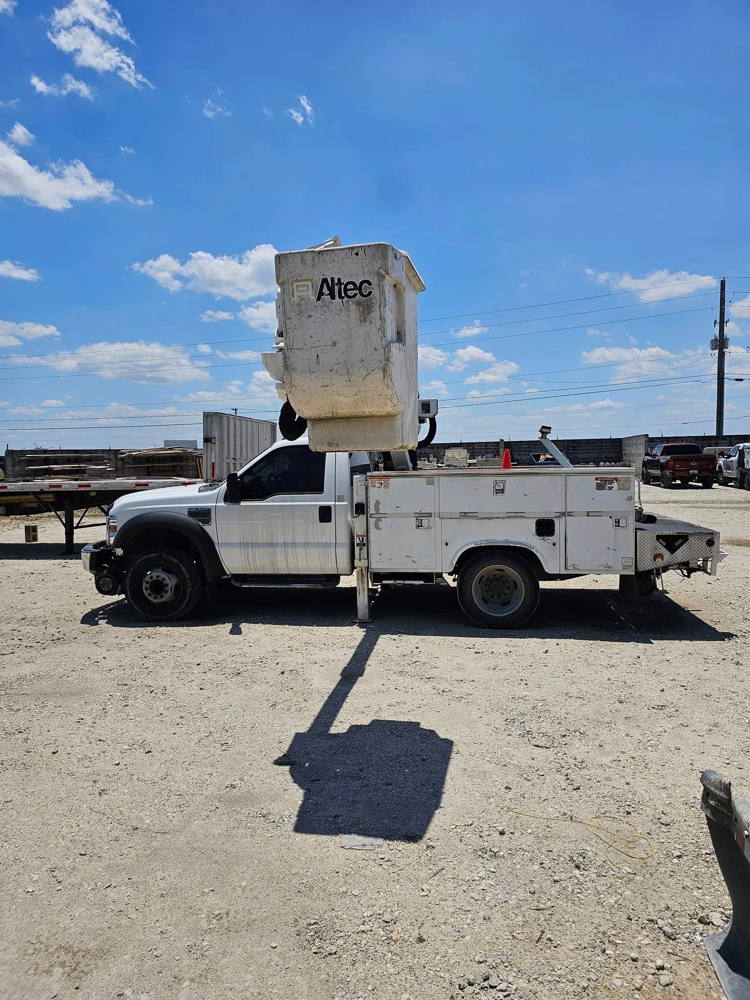 White utility truck with an elevated cargo bin parked on a gravel lot under a blue sky.