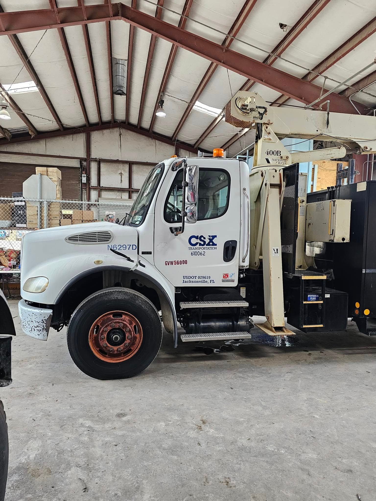 White CSX utility truck inside a warehouse, with aerial lift boom raised and equipment mounted on the rear