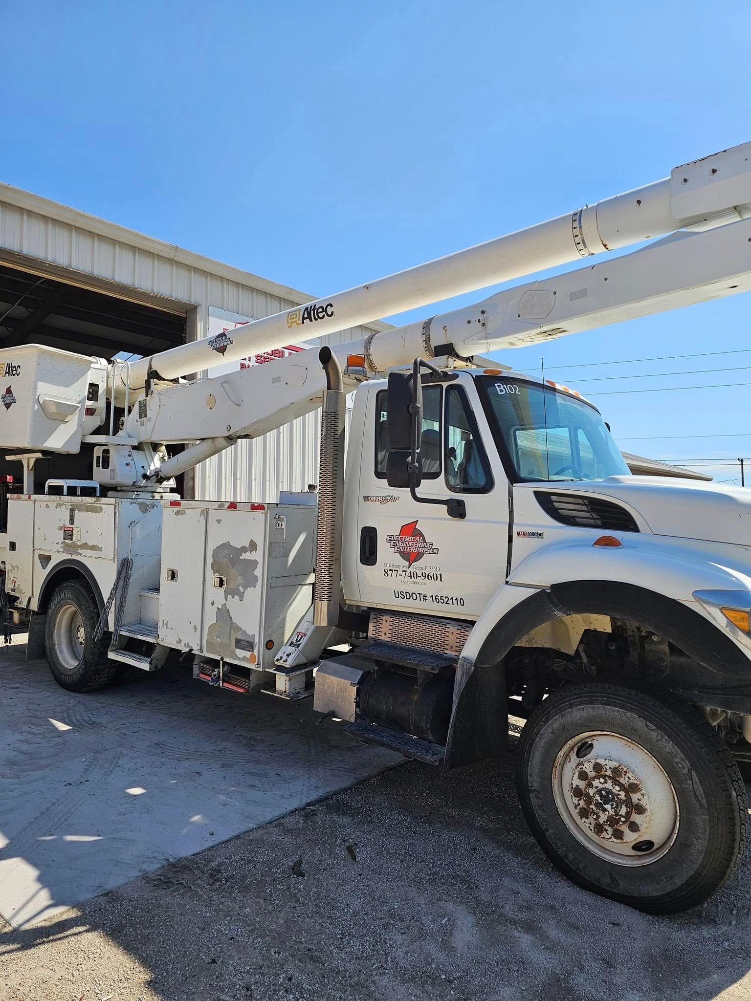 White utility bucket truck parked outdoors beside a building, with boom arm raised against a blue sky.