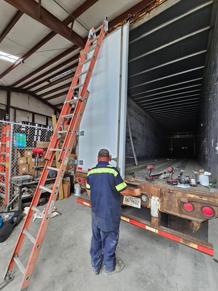 Worker unloading a white trailer in a warehouse, with an orange ladder leaning against the side.