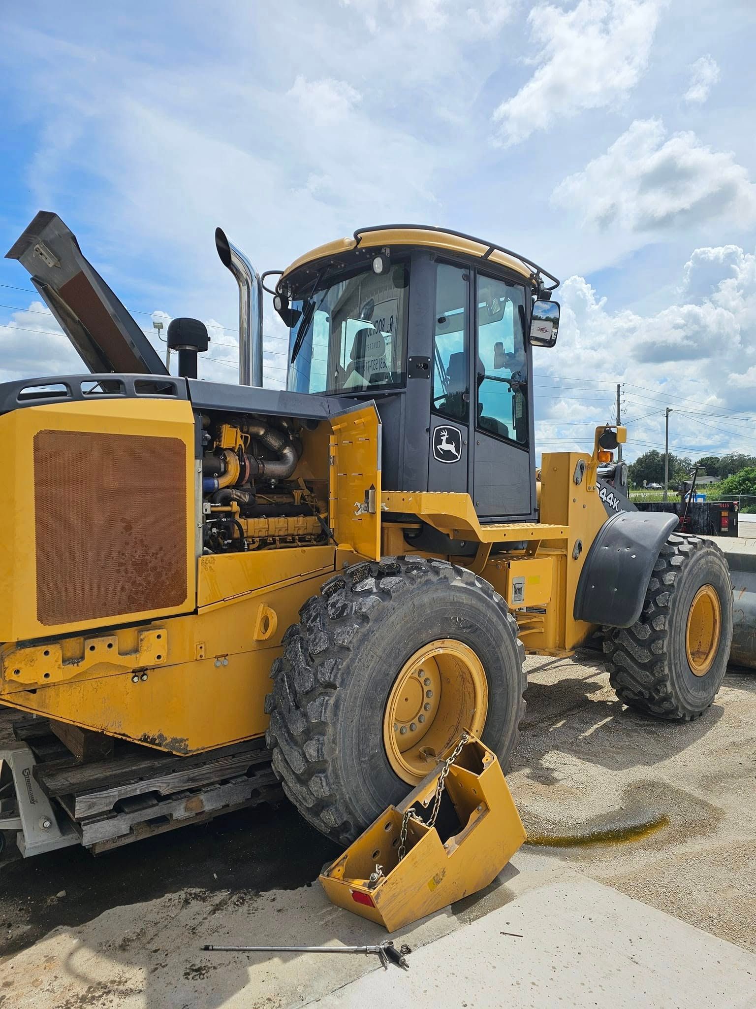 Yellow construction loader with a detached bucket, parked on a dirt lot under a cloudy sky