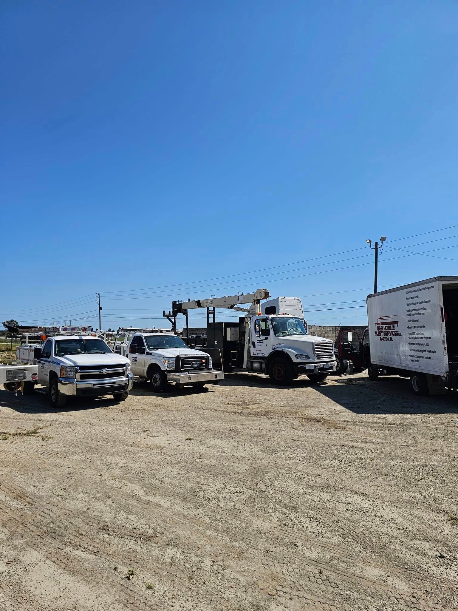 Utility trucks parked on a gravel lot under a clear blue sky, with bunting overhead.