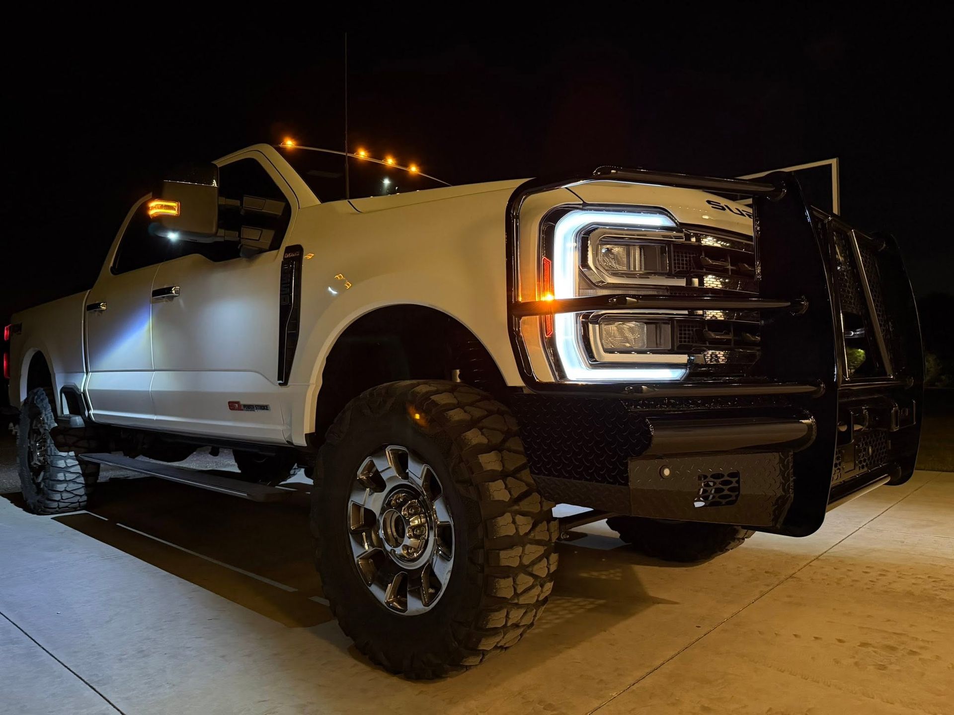 White lifted pickup truck with headlights on, parked at night under streetlights