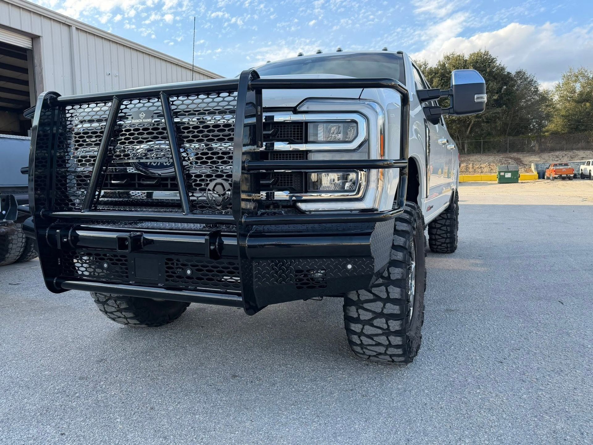 White pickup truck with heavy black grille guard and off-road tires parked outdoors on gravel