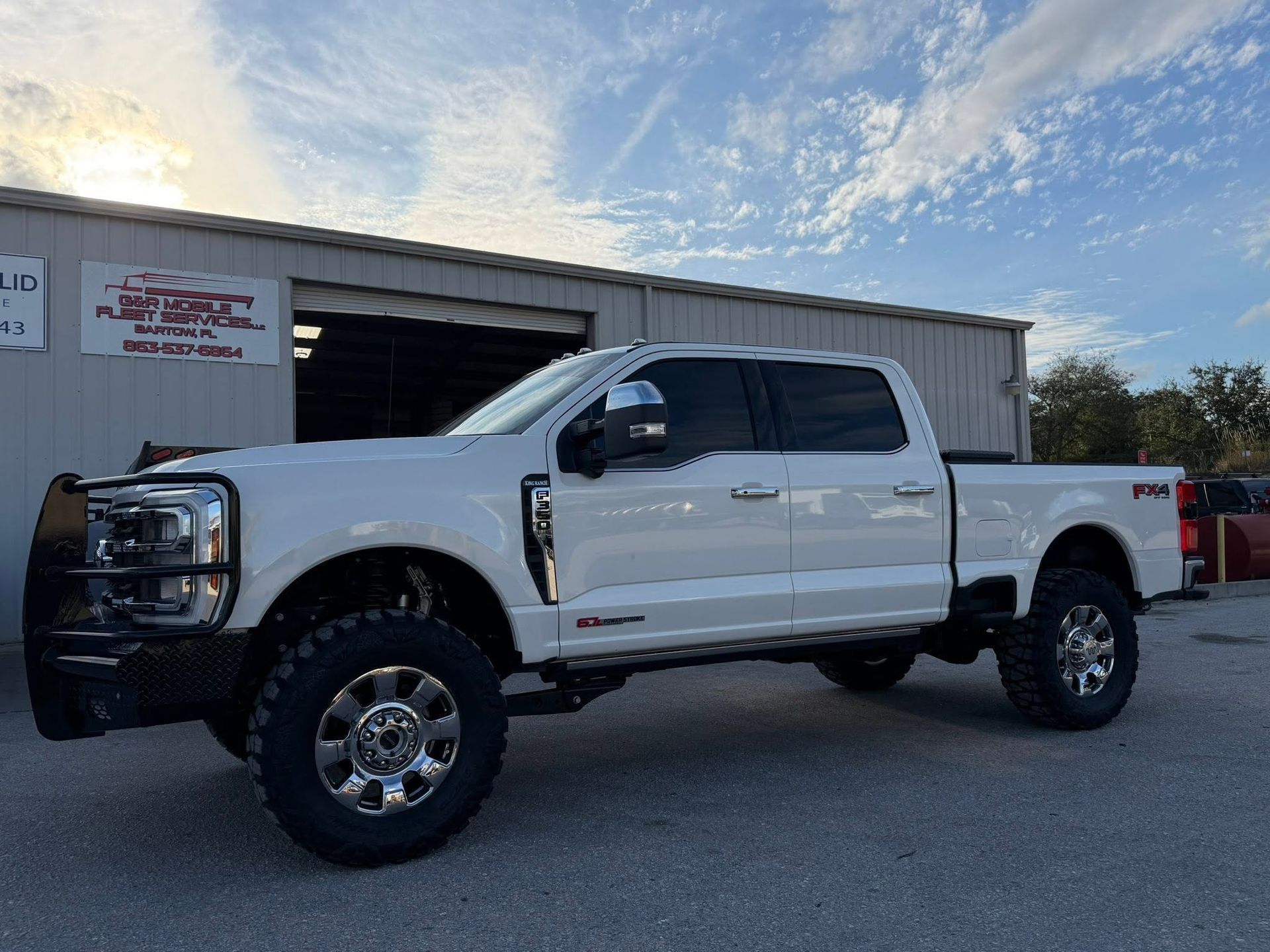 White lifted crew cab pickup truck parked outside a building on a sunny day