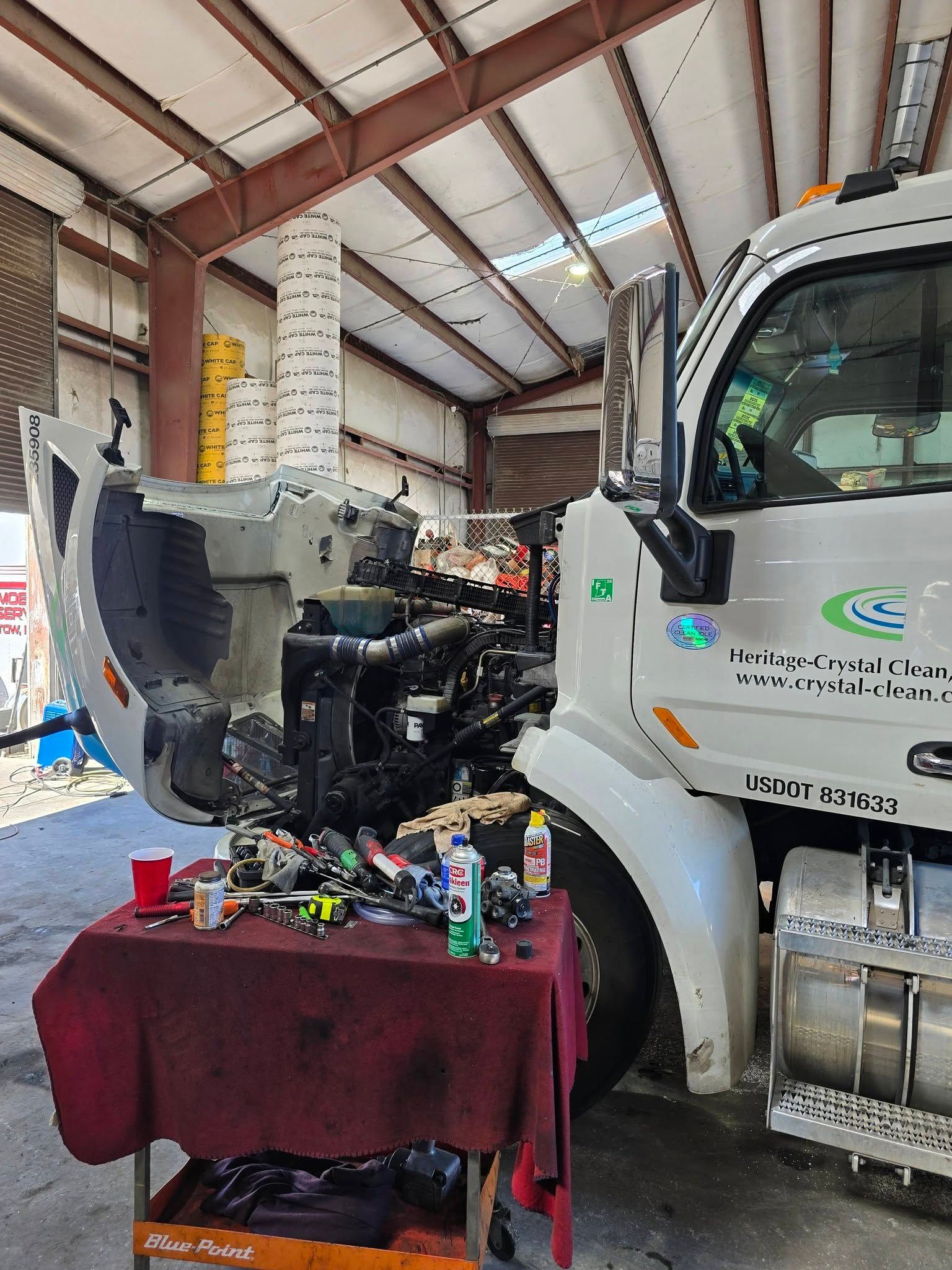 Truck repair shop with a white truck, open engine bay, and parts on a red-covered table