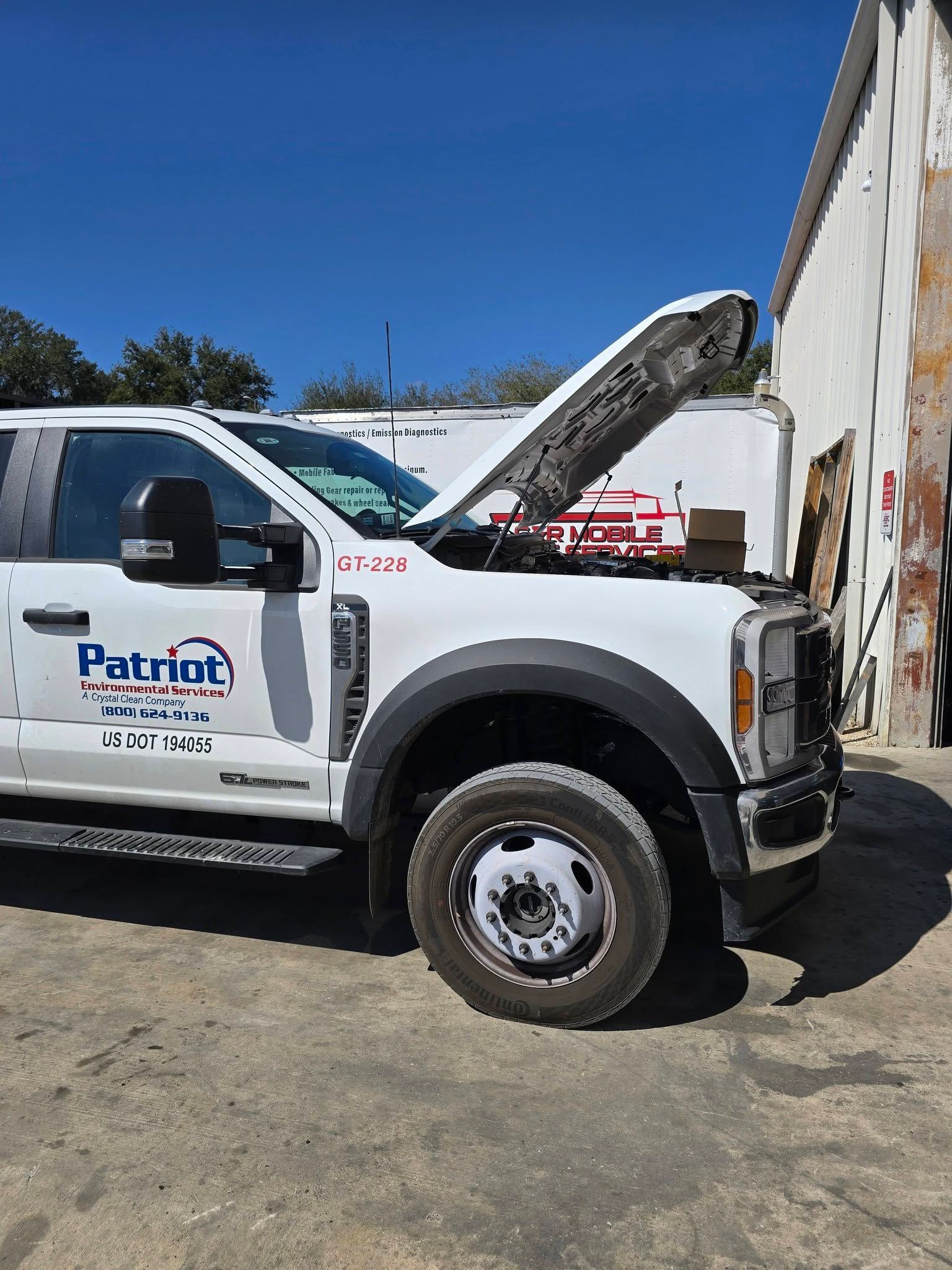 White service truck with hood open and a boom lift beside it in a sunny work yard