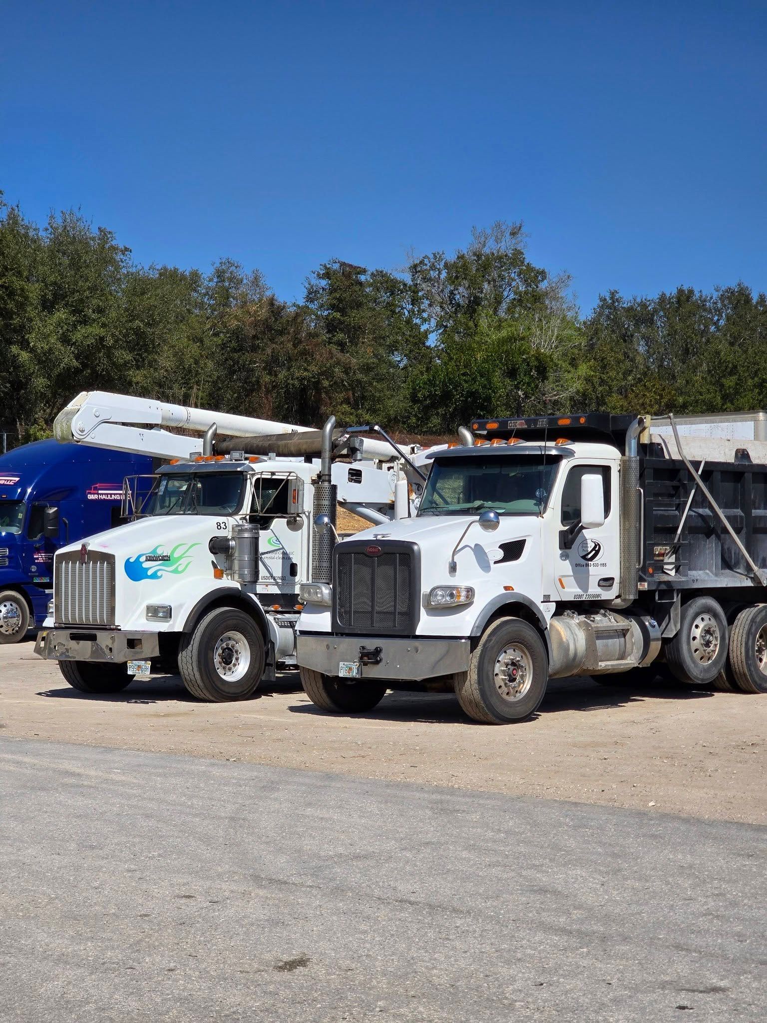 White utility trucks parked on gravel lot beside a blue truck under a clear sky