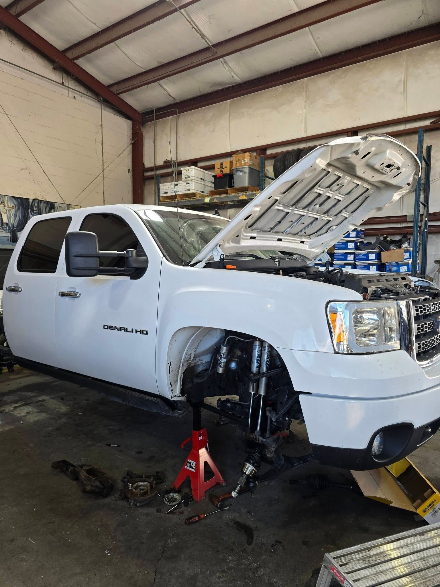 White pickup truck in a garage with hood open and front wheel removed on a jack stand