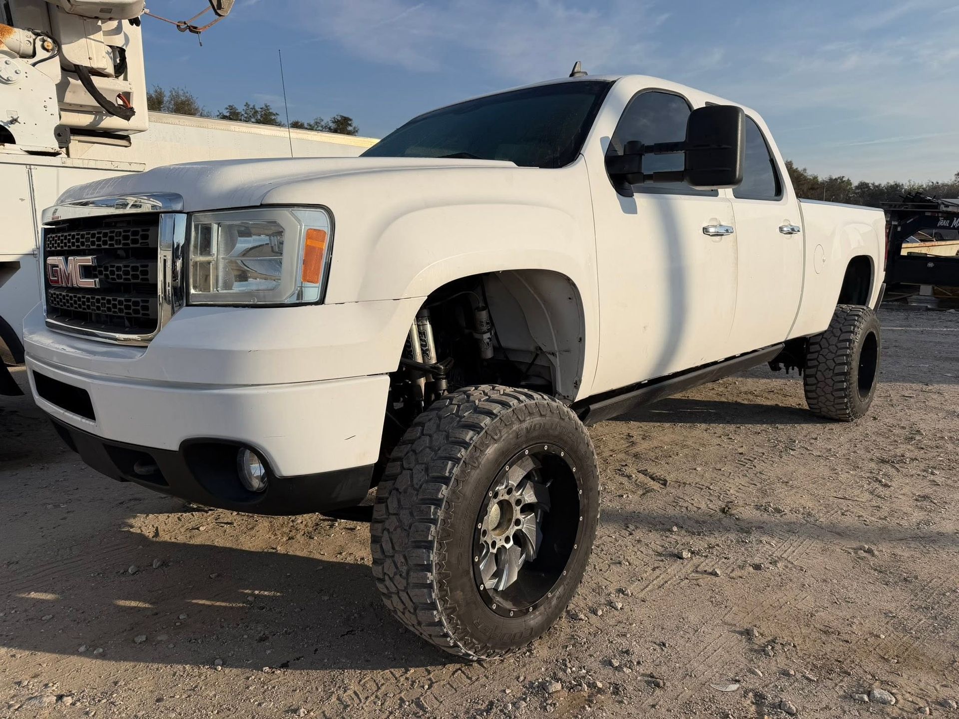 White lifted GMC pickup truck parked on gravel in a sunny desert setting