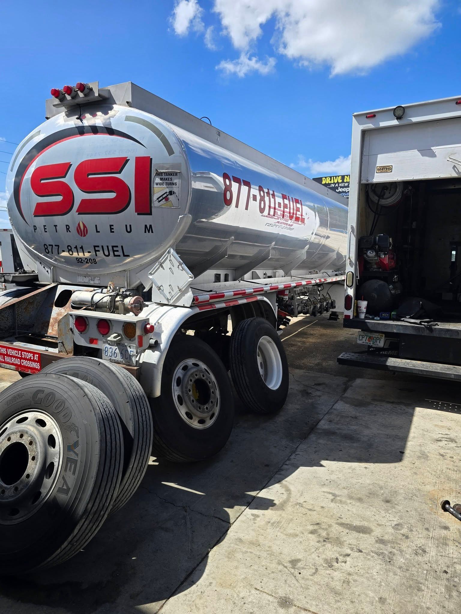 Silver SSI tanker truck parked outdoors beside another truck under a blue sky.