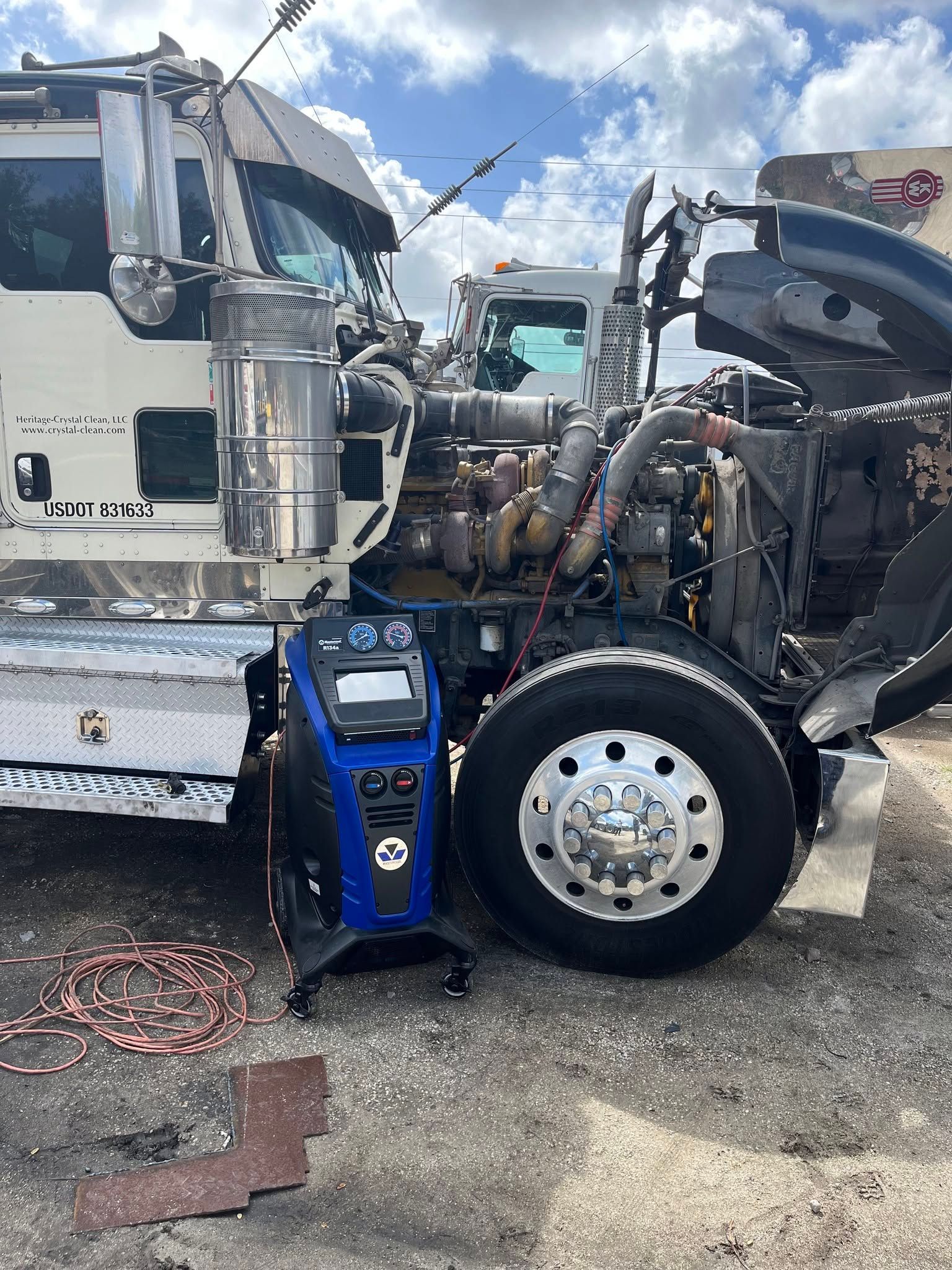 Damaged white semi-truck with exposed engine and open hood parked in a lot after a collision