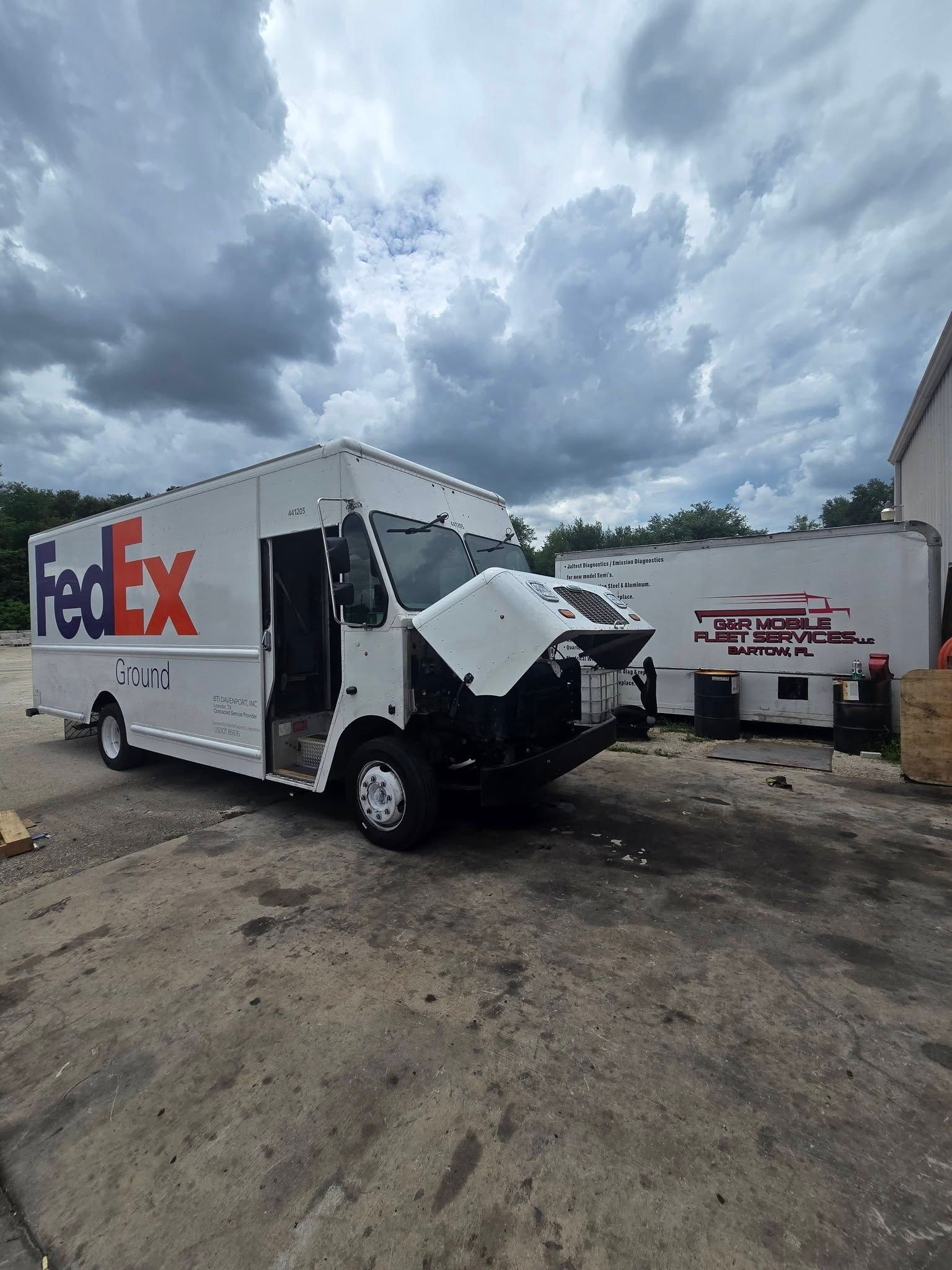 Damaged FedEx delivery truck parked beside a trailer in a muddy lot under cloudy skies