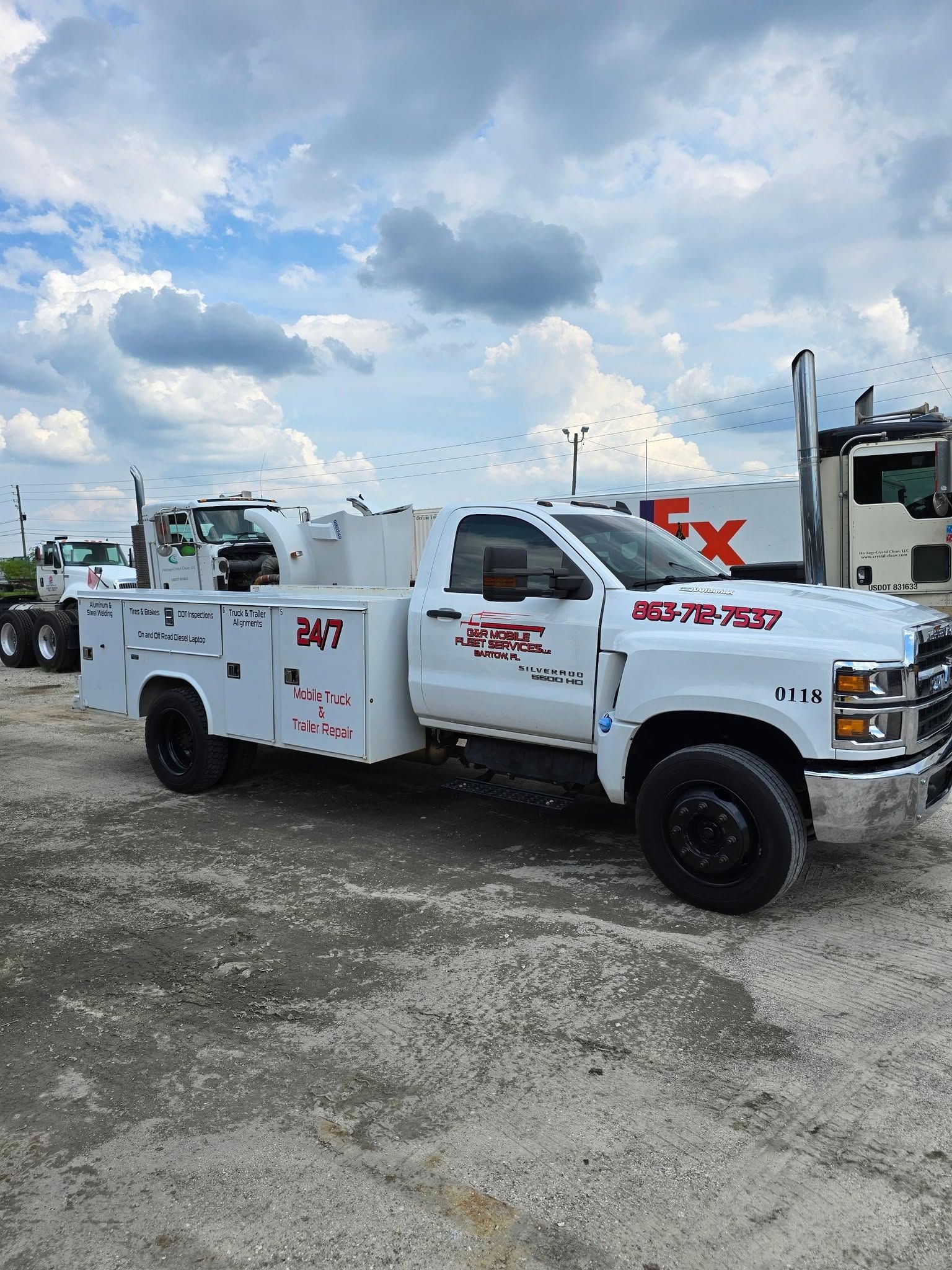 White utility truck with red lettering parked on a gravel lot under a cloudy sky