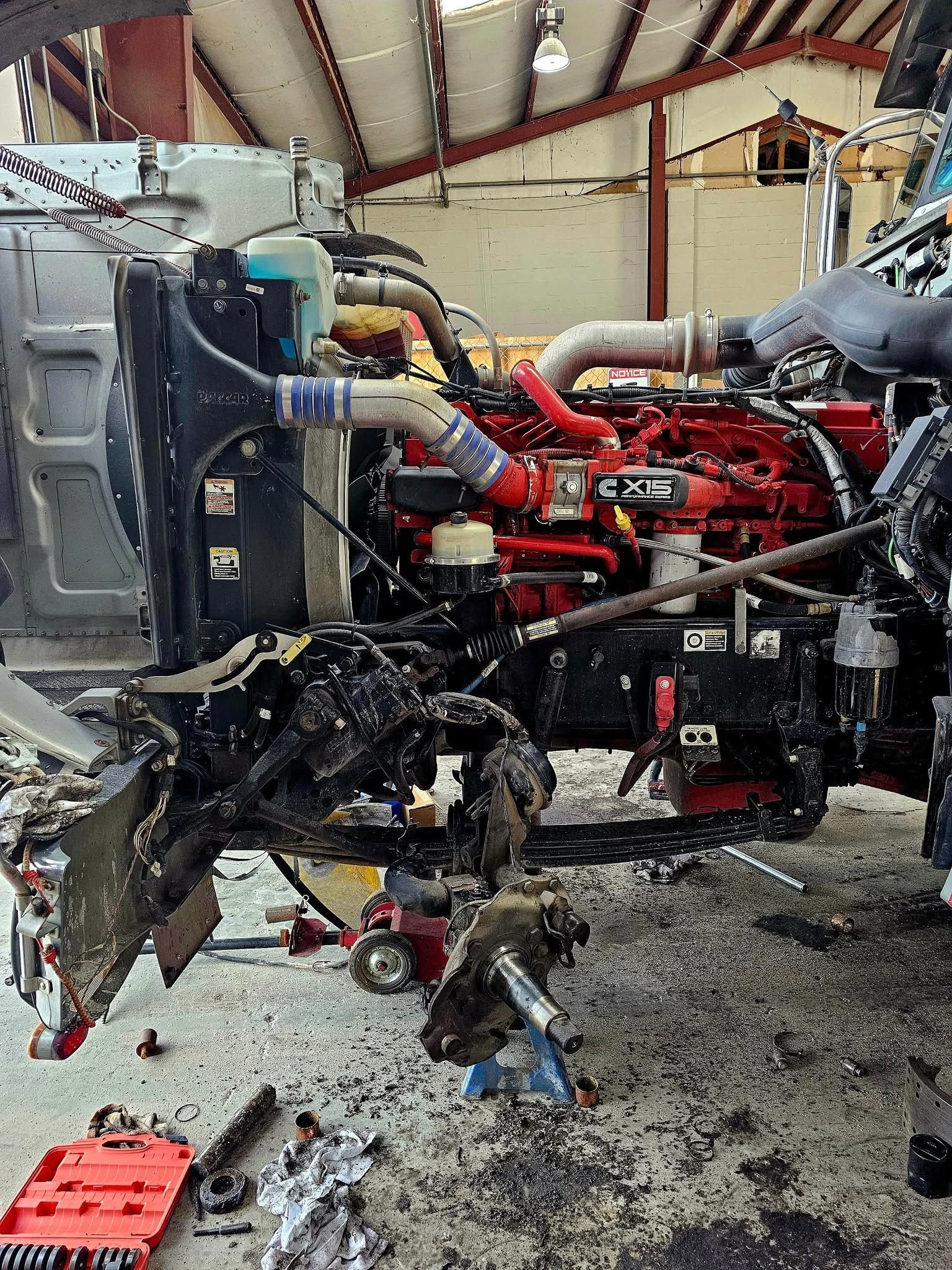 Damaged red engine and torn front end of a vehicle inside a workshop, with debris on the floor