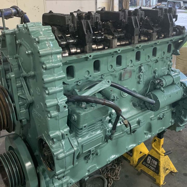 Large green industrial diesel engine on stands in a workshop, with exposed black components and hoses
