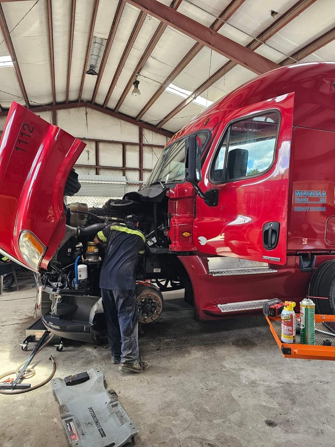 Mechanic working on a red semi-truck in a garage, hood open and tools nearby