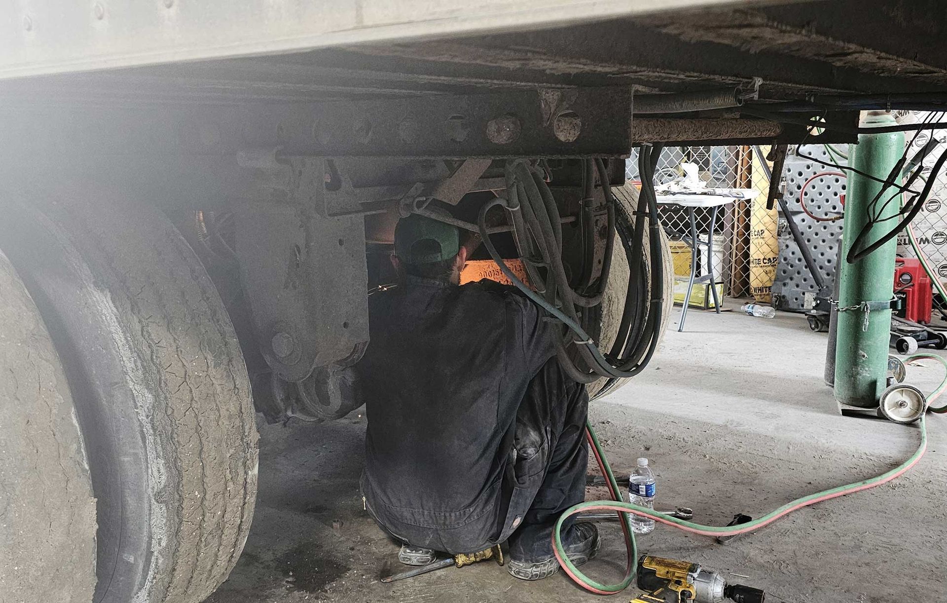 Mechanic working beneath a truck, surrounded by hoses and tools in a garage bay