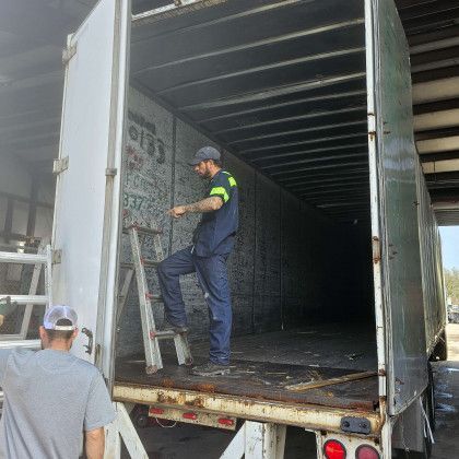 Worker climbing a ladder into an open cargo truck while another stands nearby in a loading area